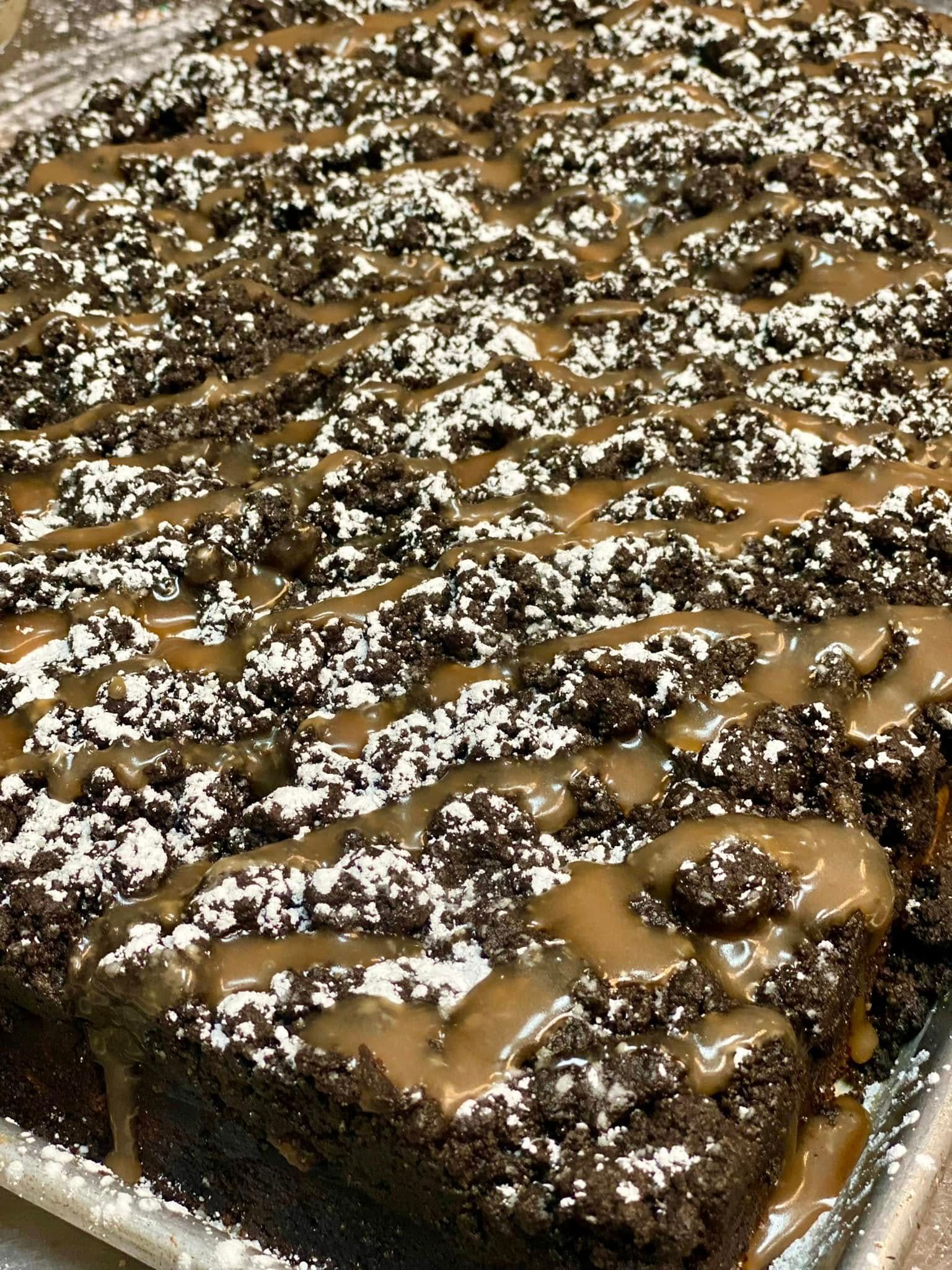 Chocolate cake topped with crumbly frosting, caramel drizzle, and powdered sugar.