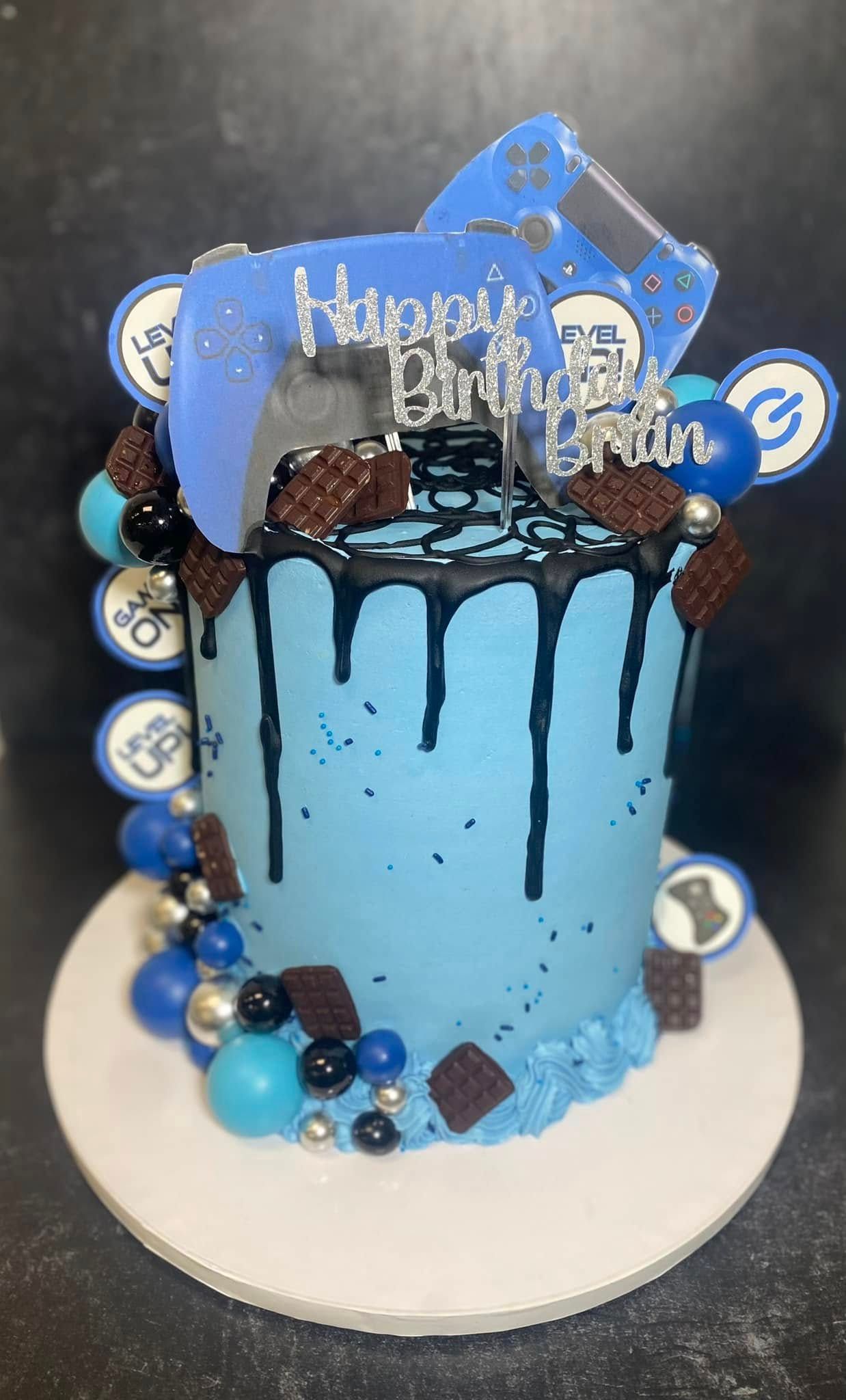 Blue birthday cake with a gaming theme, including controller and chocolate decorations.