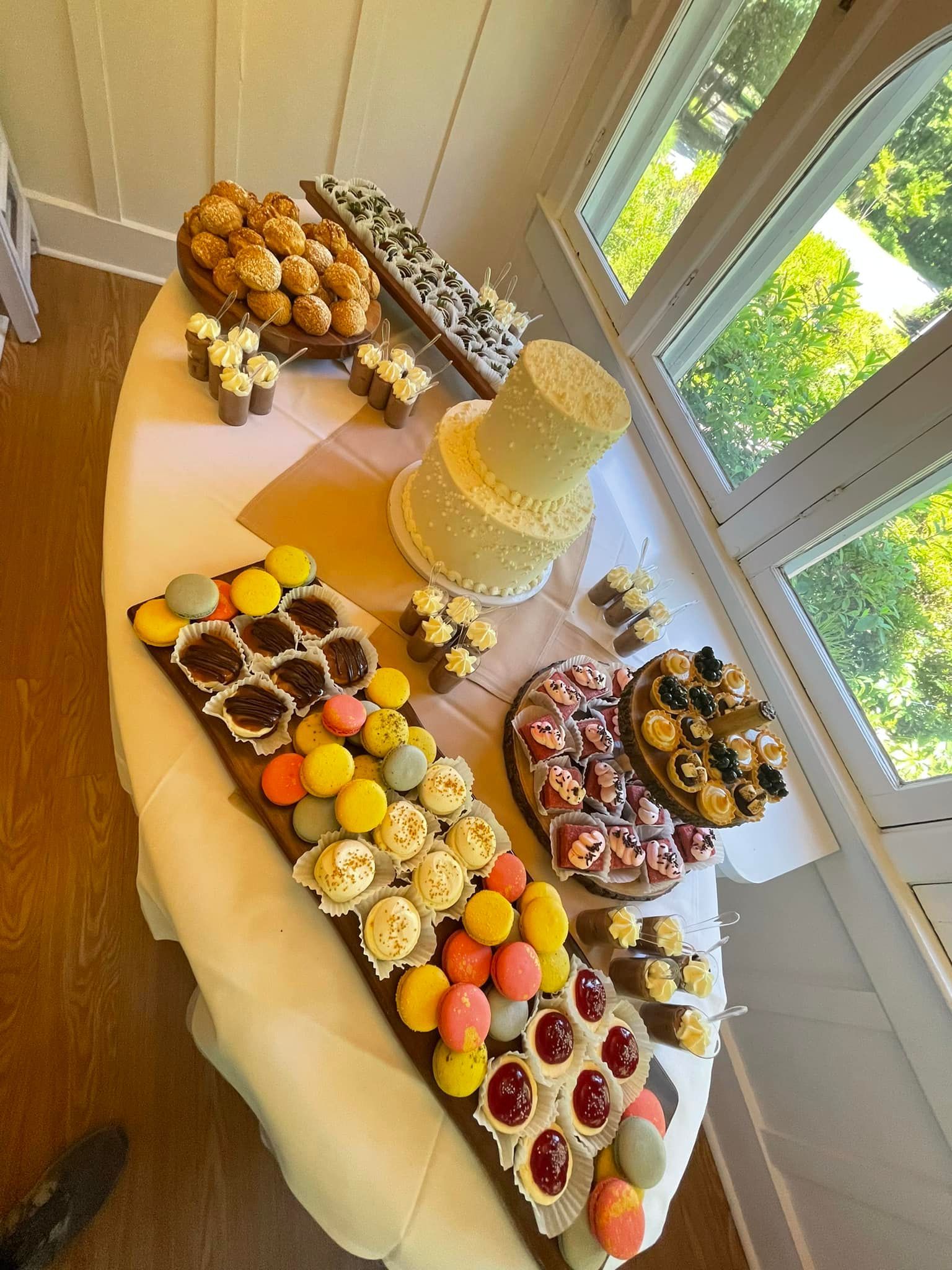 Dessert table: Cake, cupcakes, macarons, mini tarts on a round white table, near a window.