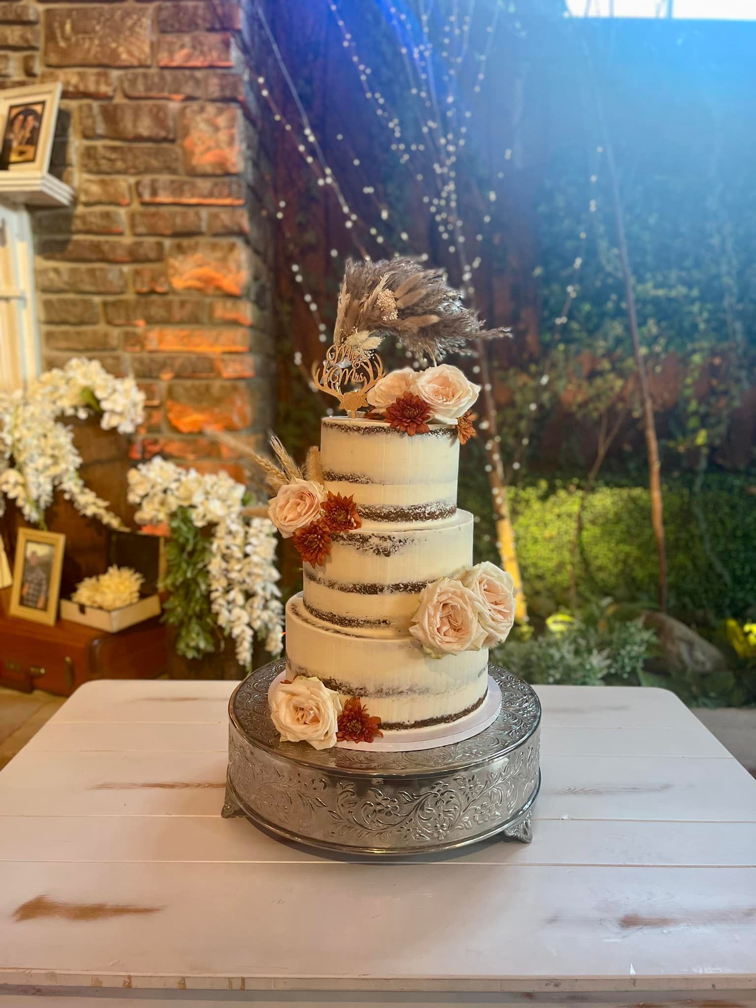Four-tier wedding cake with floral decorations on a white table in a decorated setting.