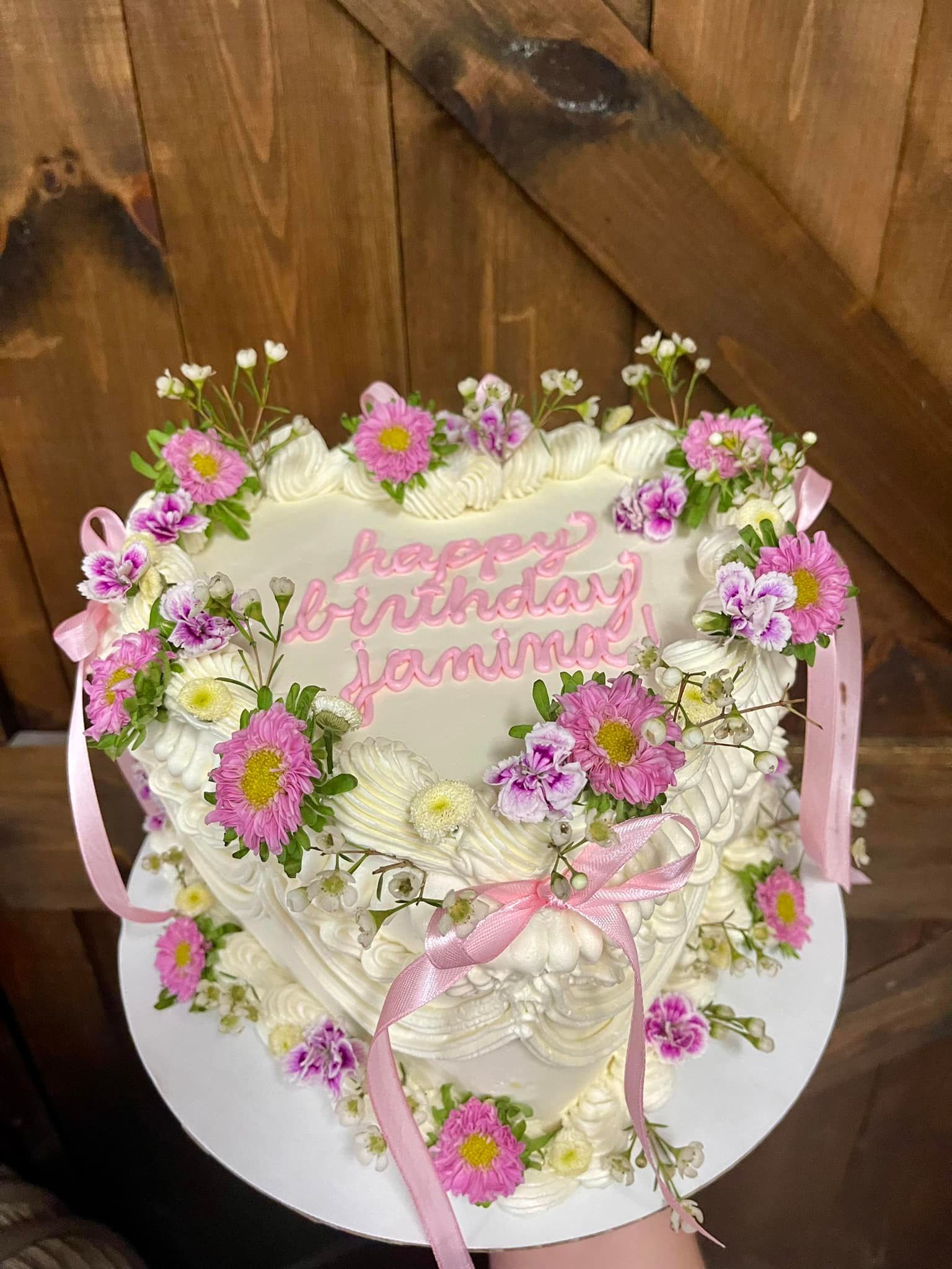 Heart-shaped cake decorated with pink flowers and a pink ribbon, with 