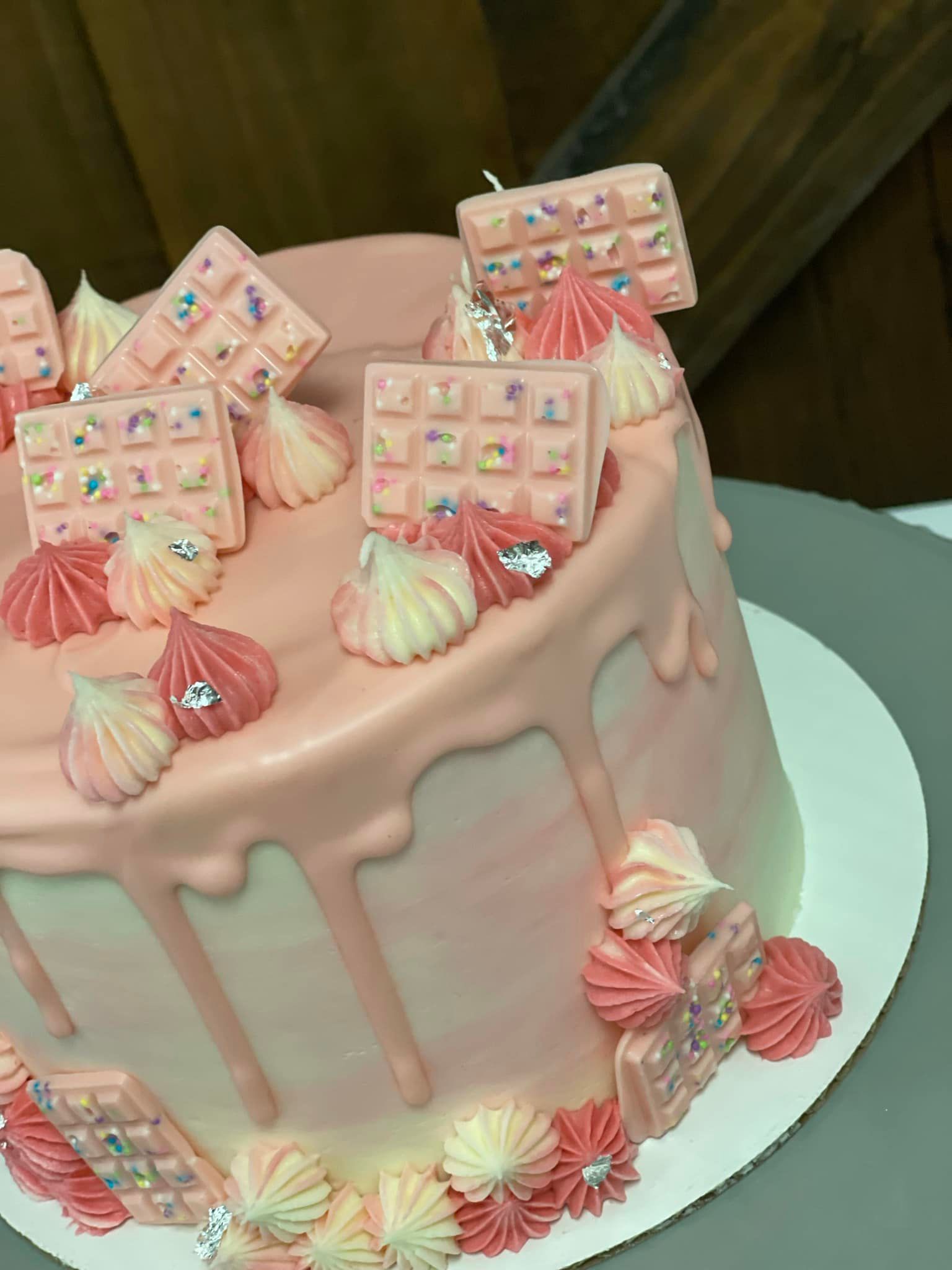 Pink cake with chocolate squares, meringues, and sprinkles.