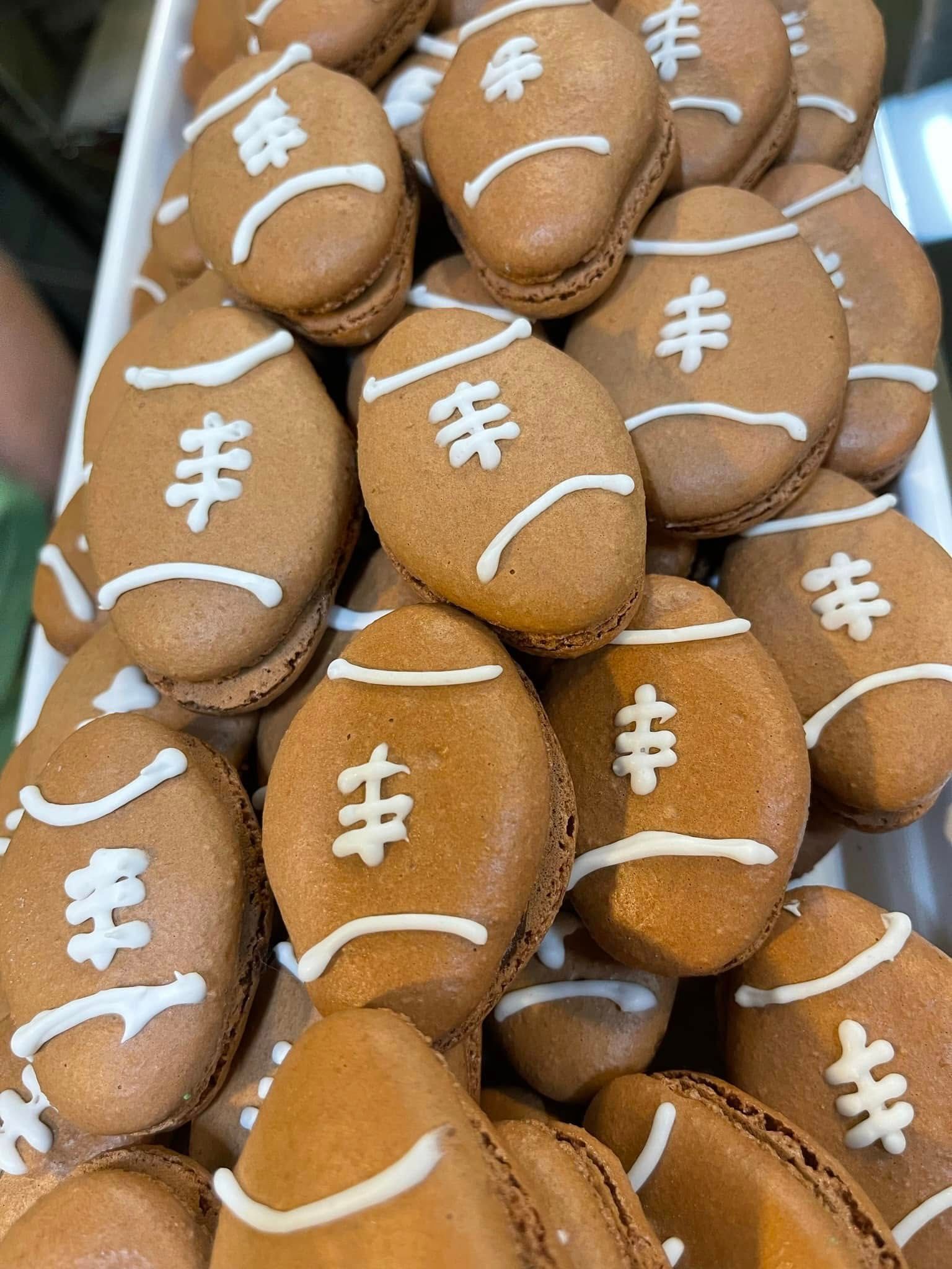 Football-shaped macarons in a tray, brown with white icing details.