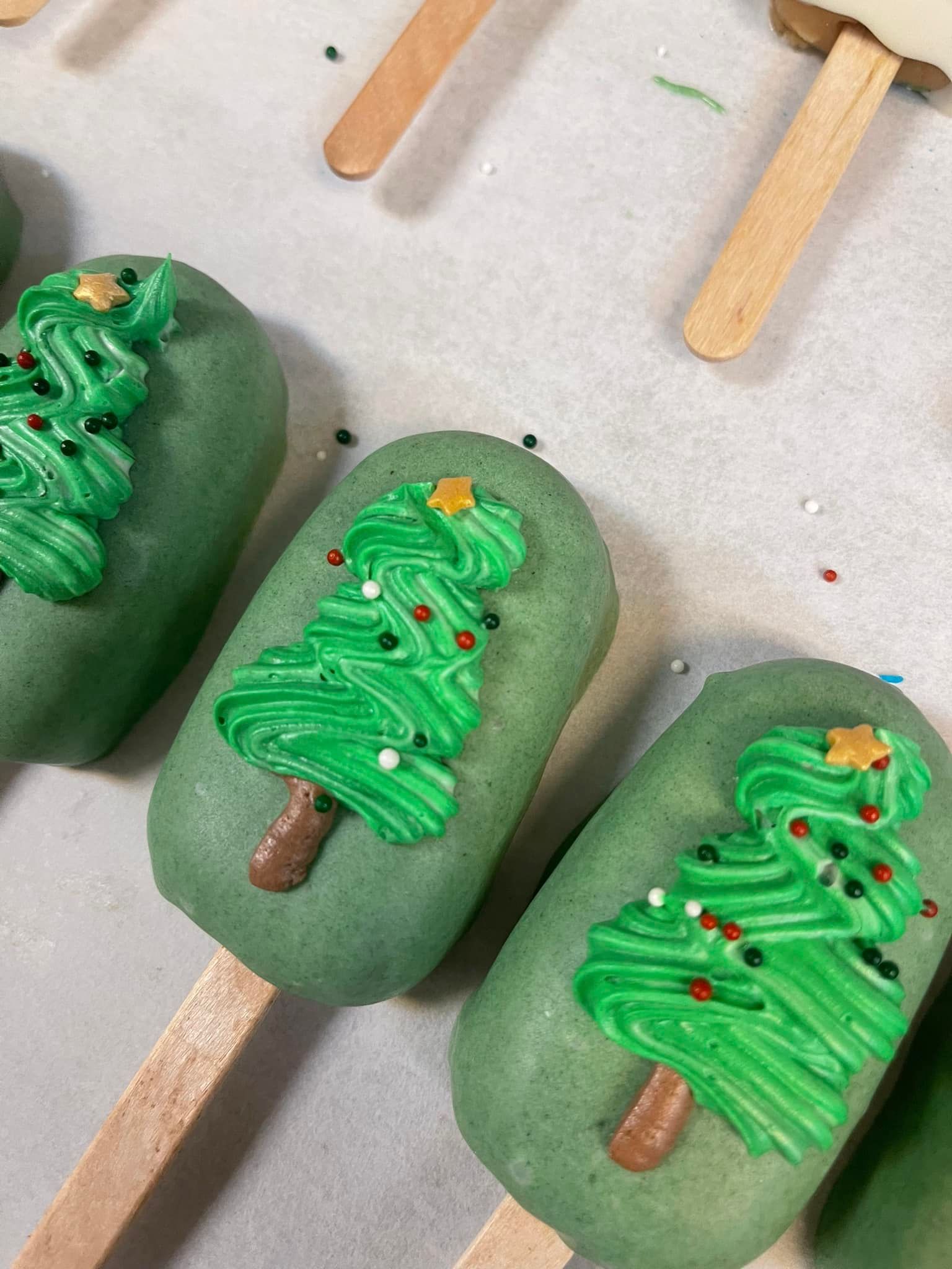 Green cake pops shaped as Christmas trees, decorated with green frosting, sprinkles, and a star.