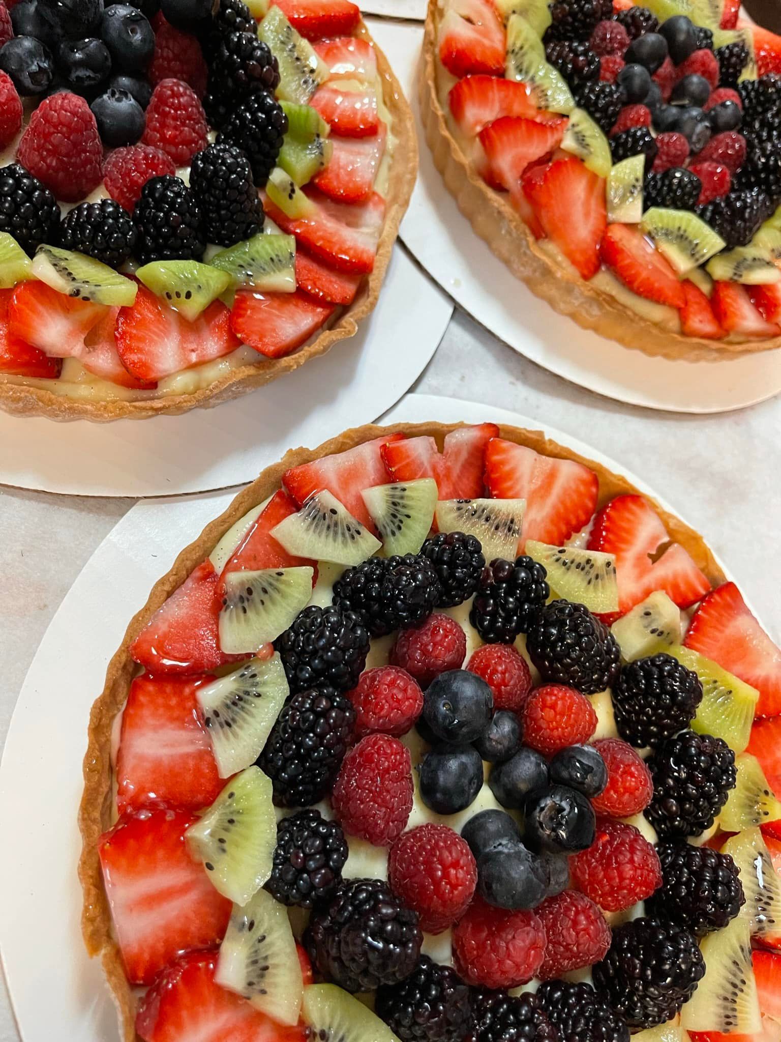 Fruit tarts with strawberries, kiwi, blackberries, raspberries, and blueberries arranged on white plates.