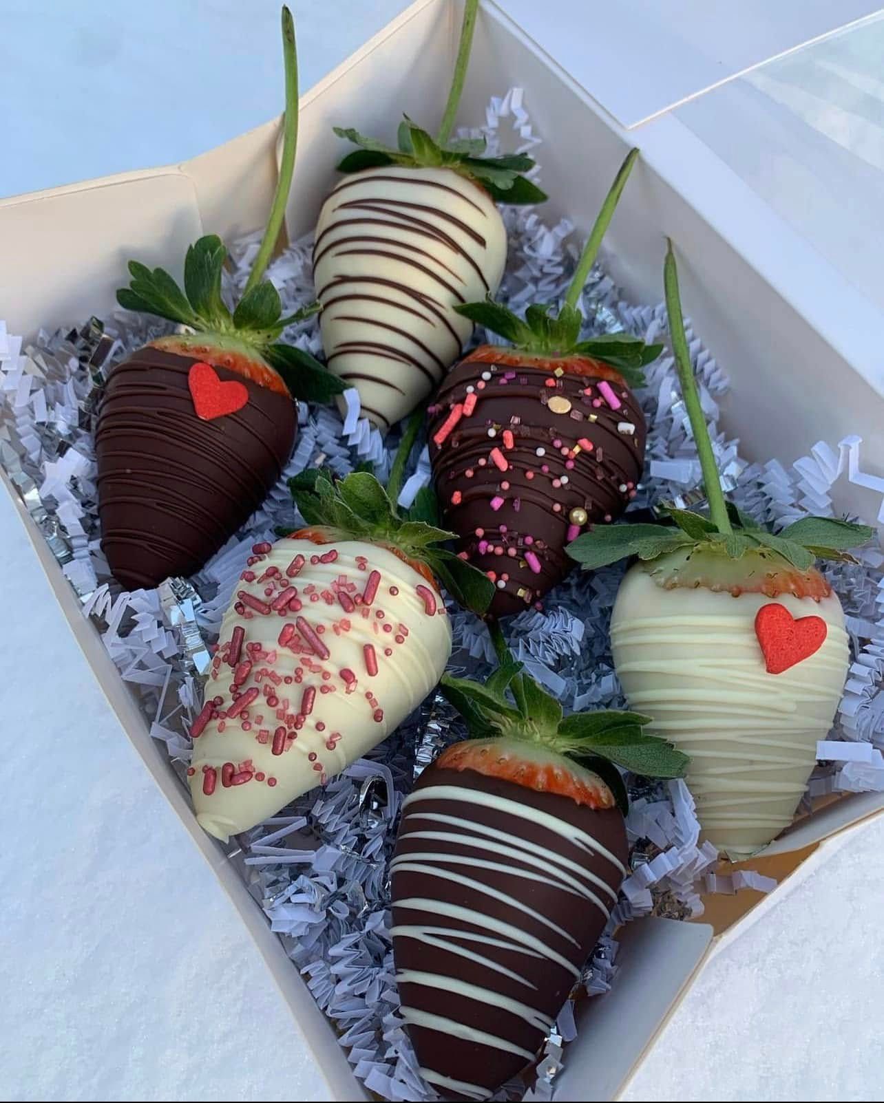 Chocolate-covered strawberries in a white box with decorative paper, various colors and designs, perfect for gifting.