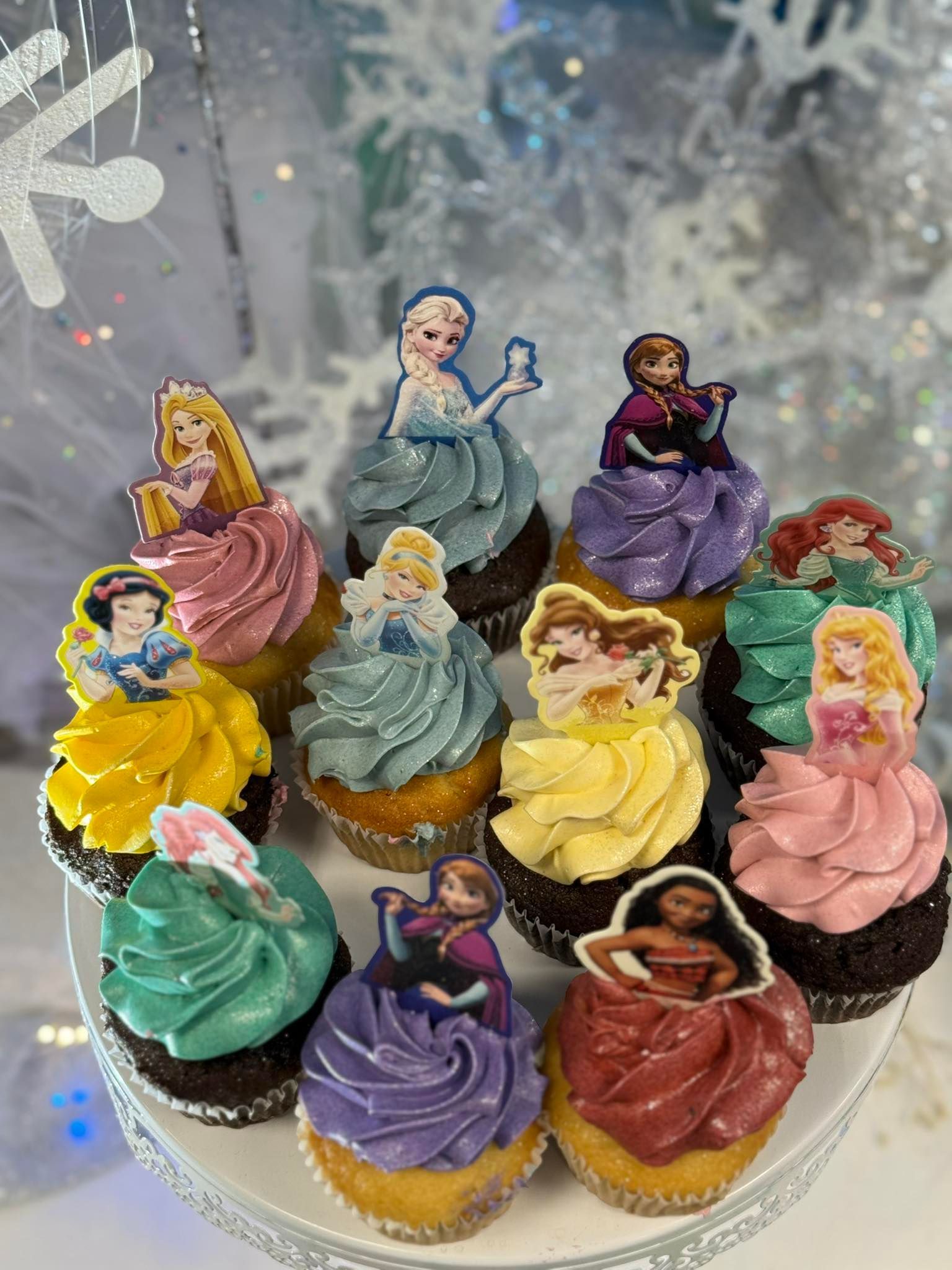 Cupcakes topped with Disney princess figurines on a white tiered platter.