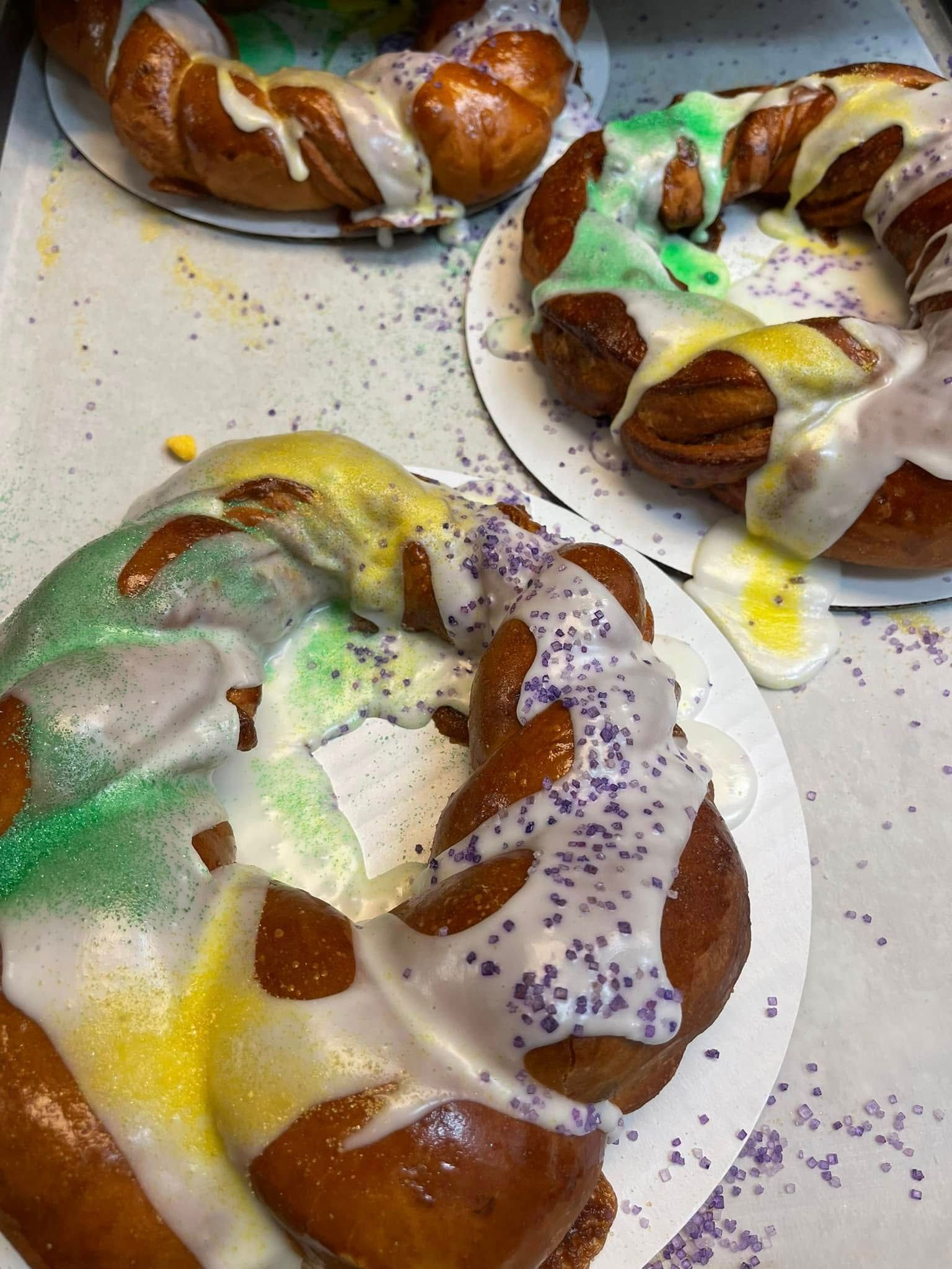 King cakes with purple, green, and yellow icing and sprinkles on a counter.