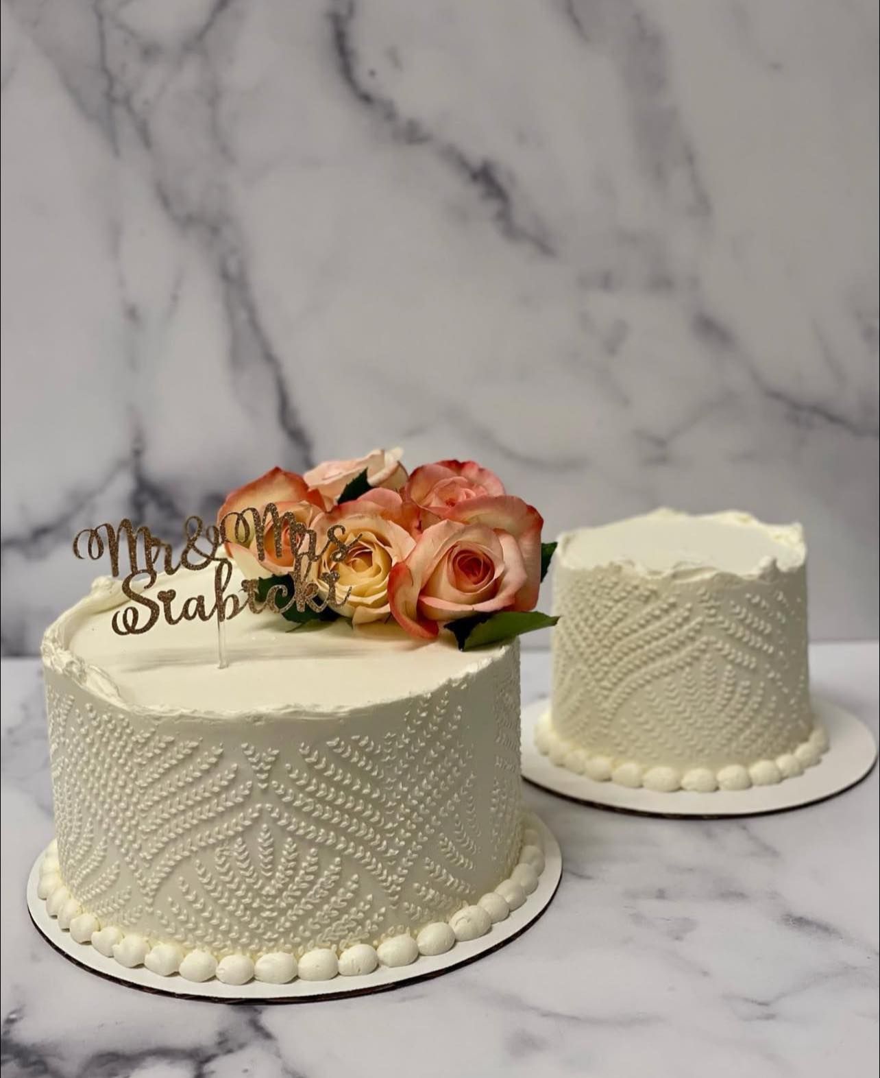 Two-tiered wedding cakes with ivory textured frosting, floral topper, and 
