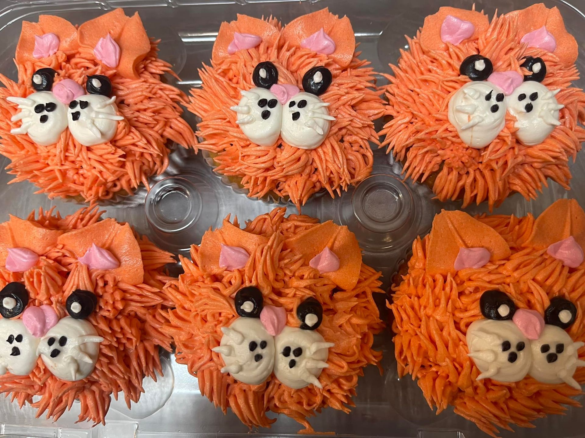 Orange cat-shaped cupcakes decorated with orange frosting, white frosting features, and black eyes.