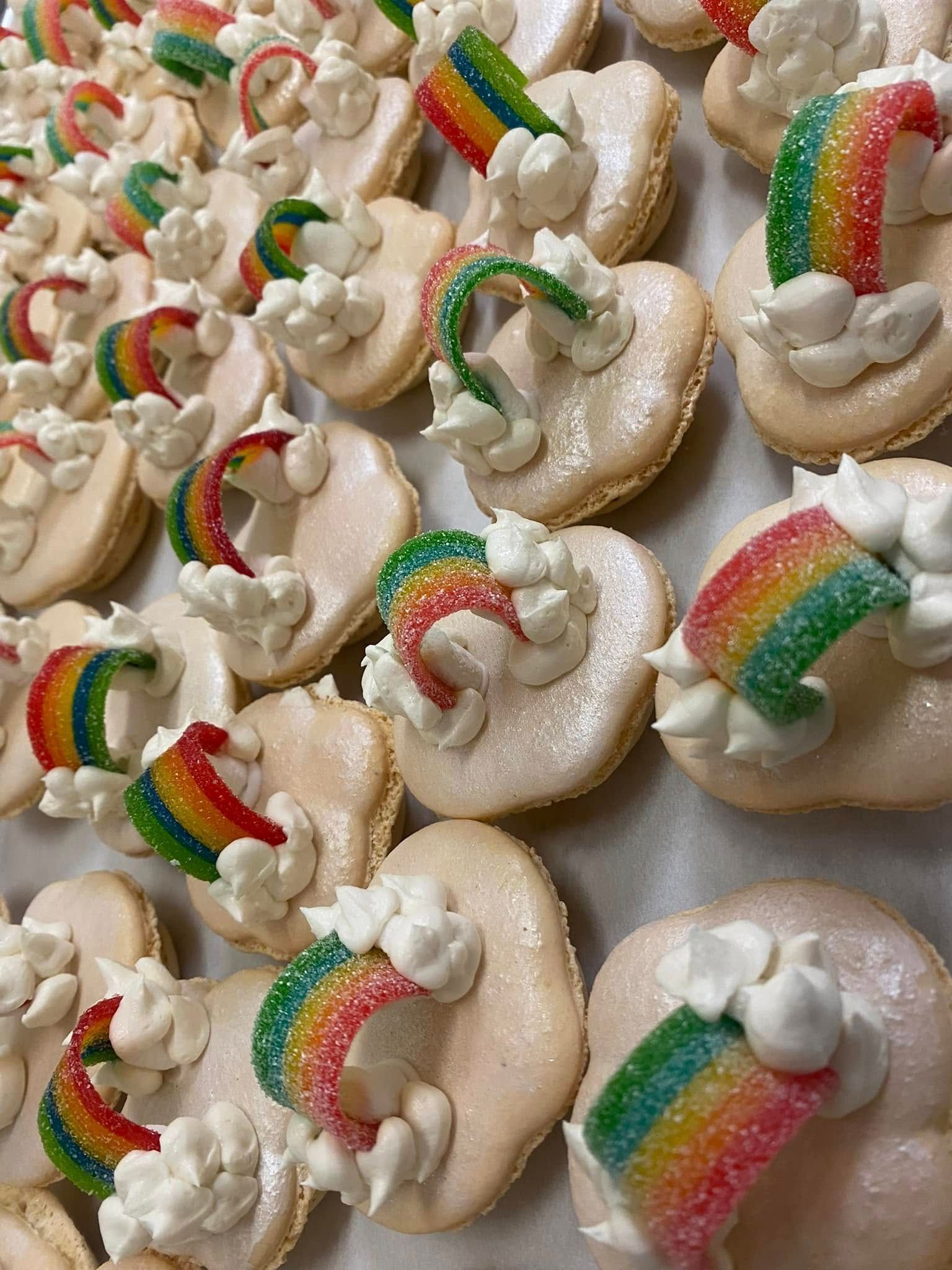 Heart-shaped macarons, decorated with white frosting clouds and rainbow candy arcs.