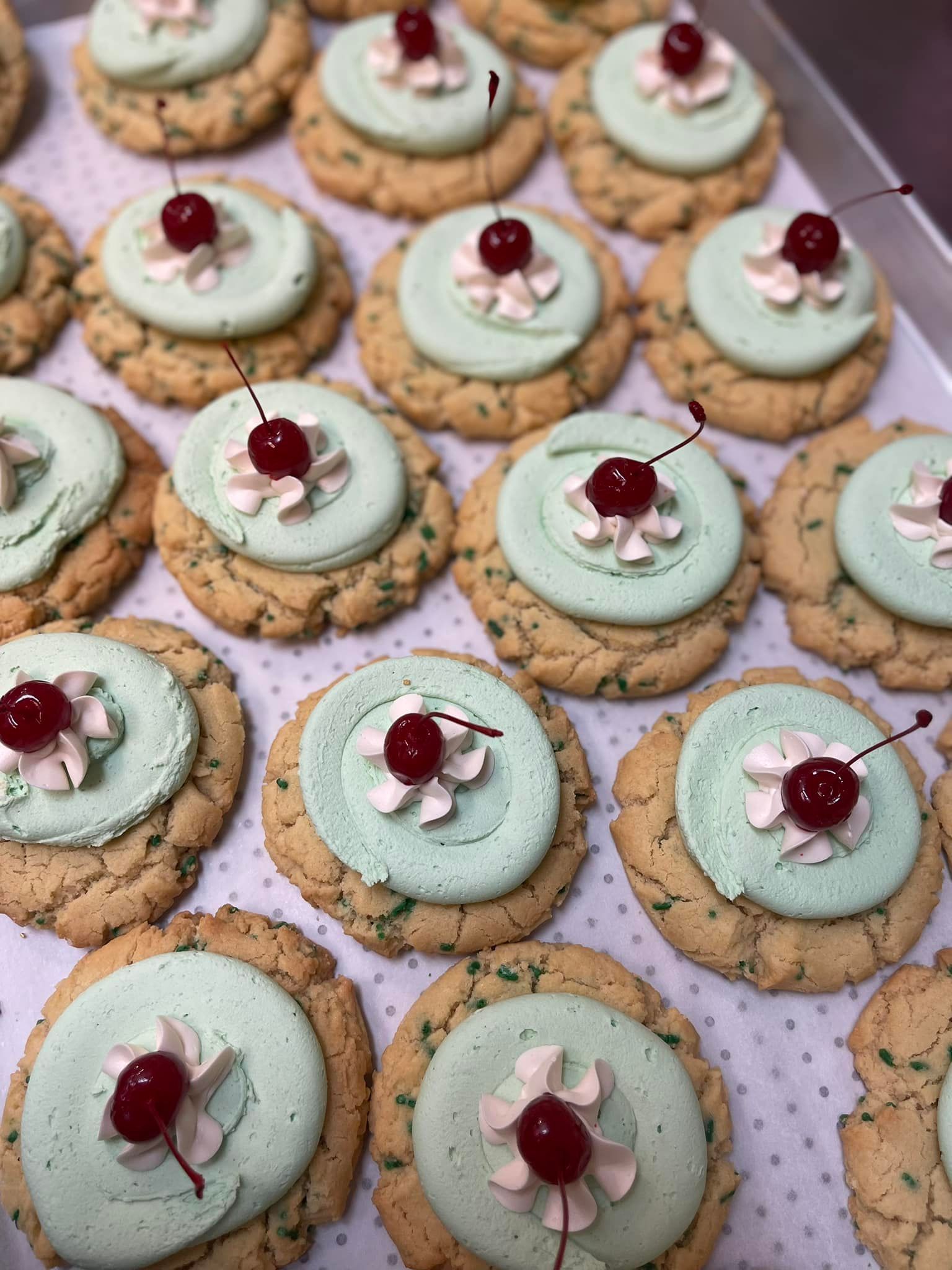 Cookies topped with pale green frosting and a cherry.