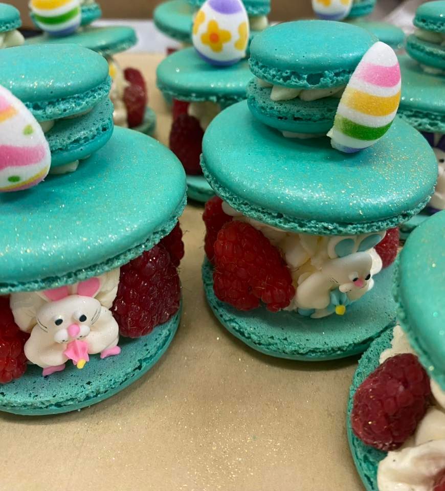 Teal macarons with white cream, raspberries, and Easter bunny and egg decorations.