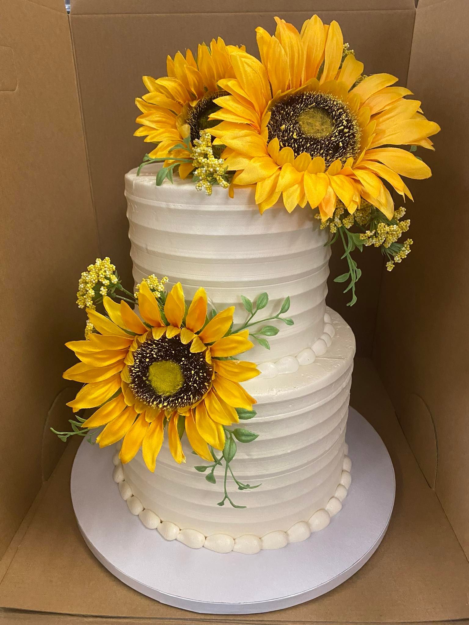 Two-tiered cake decorated with yellow sunflowers and greenery.