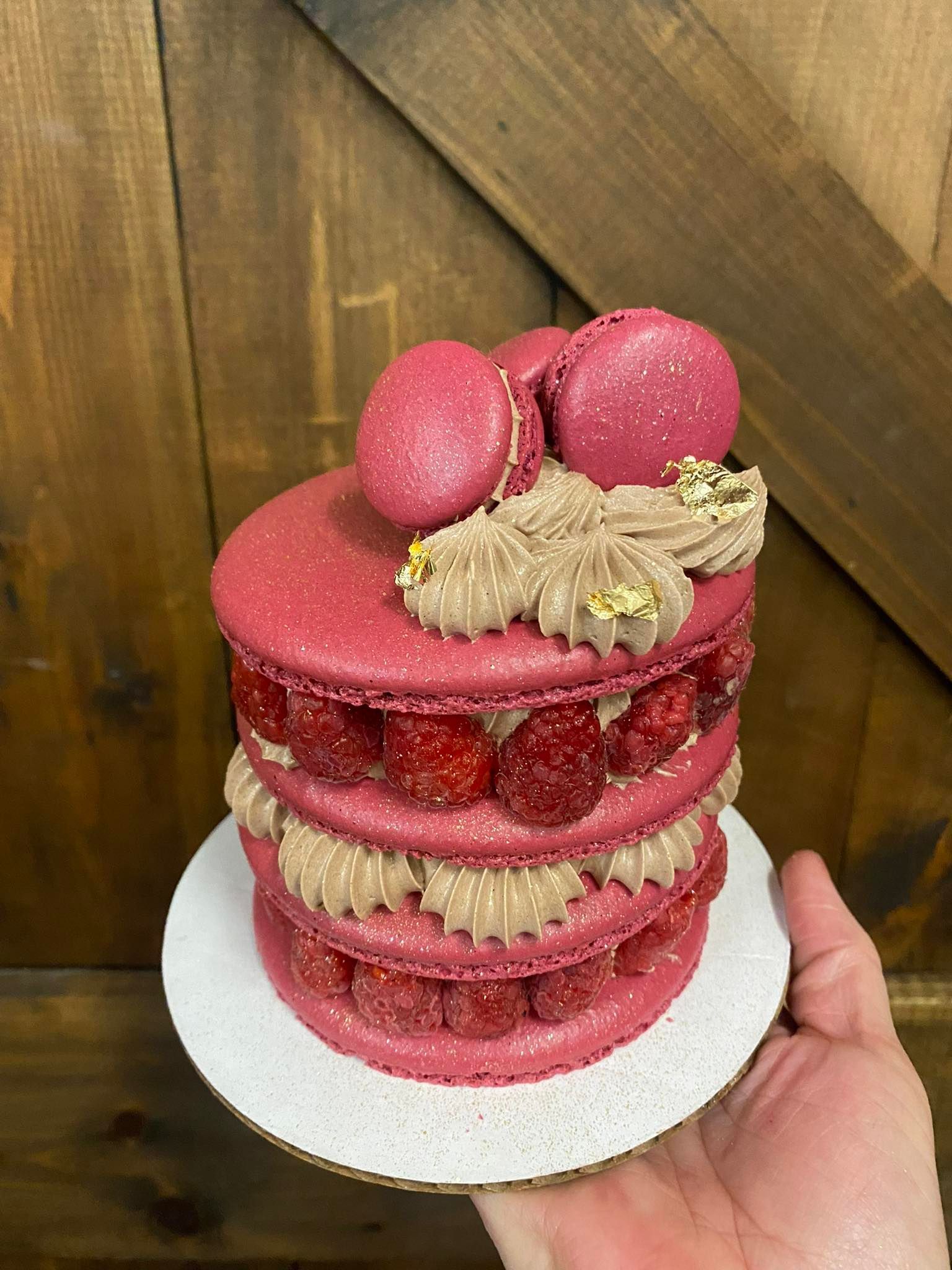 Macaron cake with pink shells, raspberry filling, and brown frosting on a white plate.