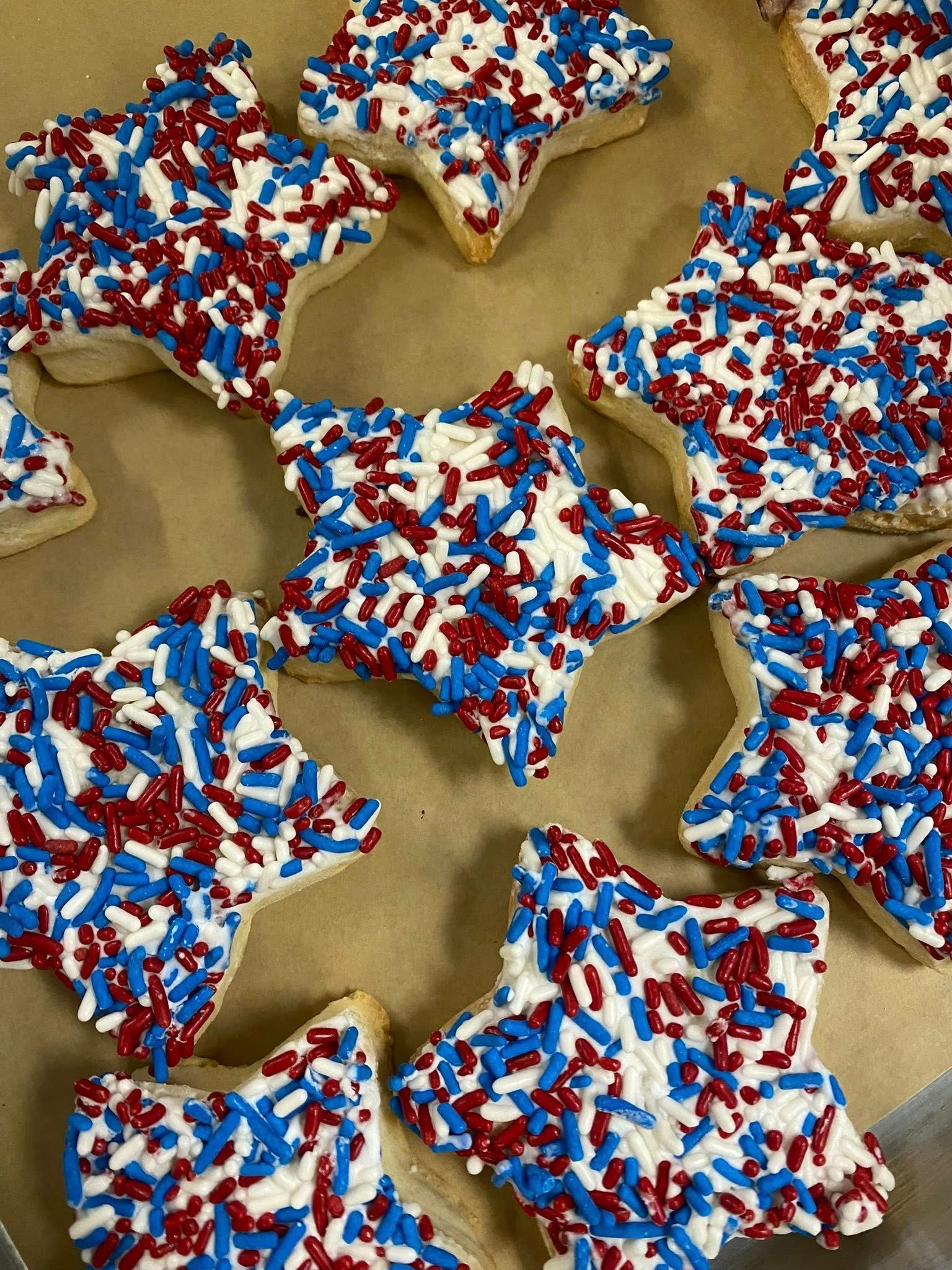 Star-shaped sugar cookies decorated with red, white, and blue sprinkles on parchment paper.