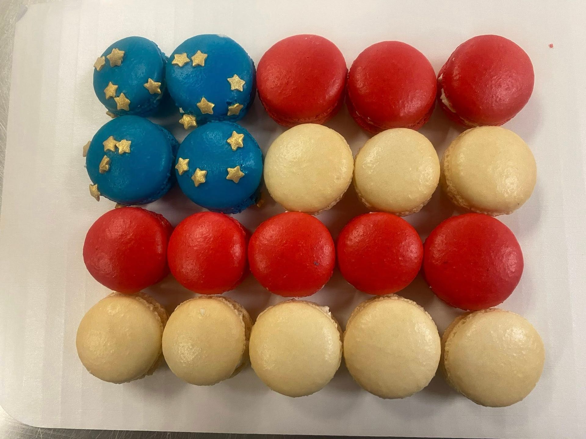Rows of red, white, and blue macarons arranged to resemble an American flag. Blue ones have gold star sprinkles.