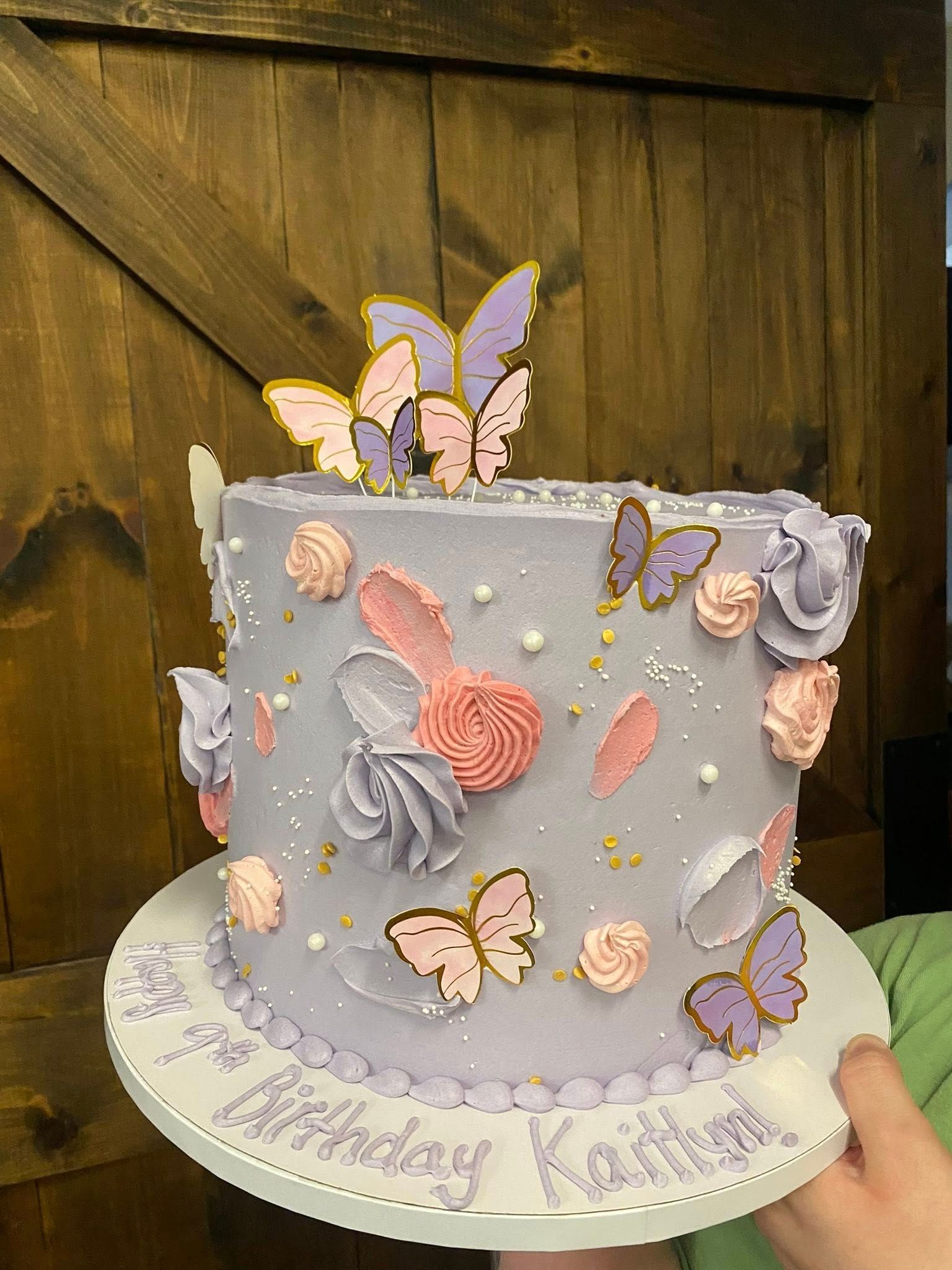 A decorated birthday cake with butterfly and flower designs on a white cake board.