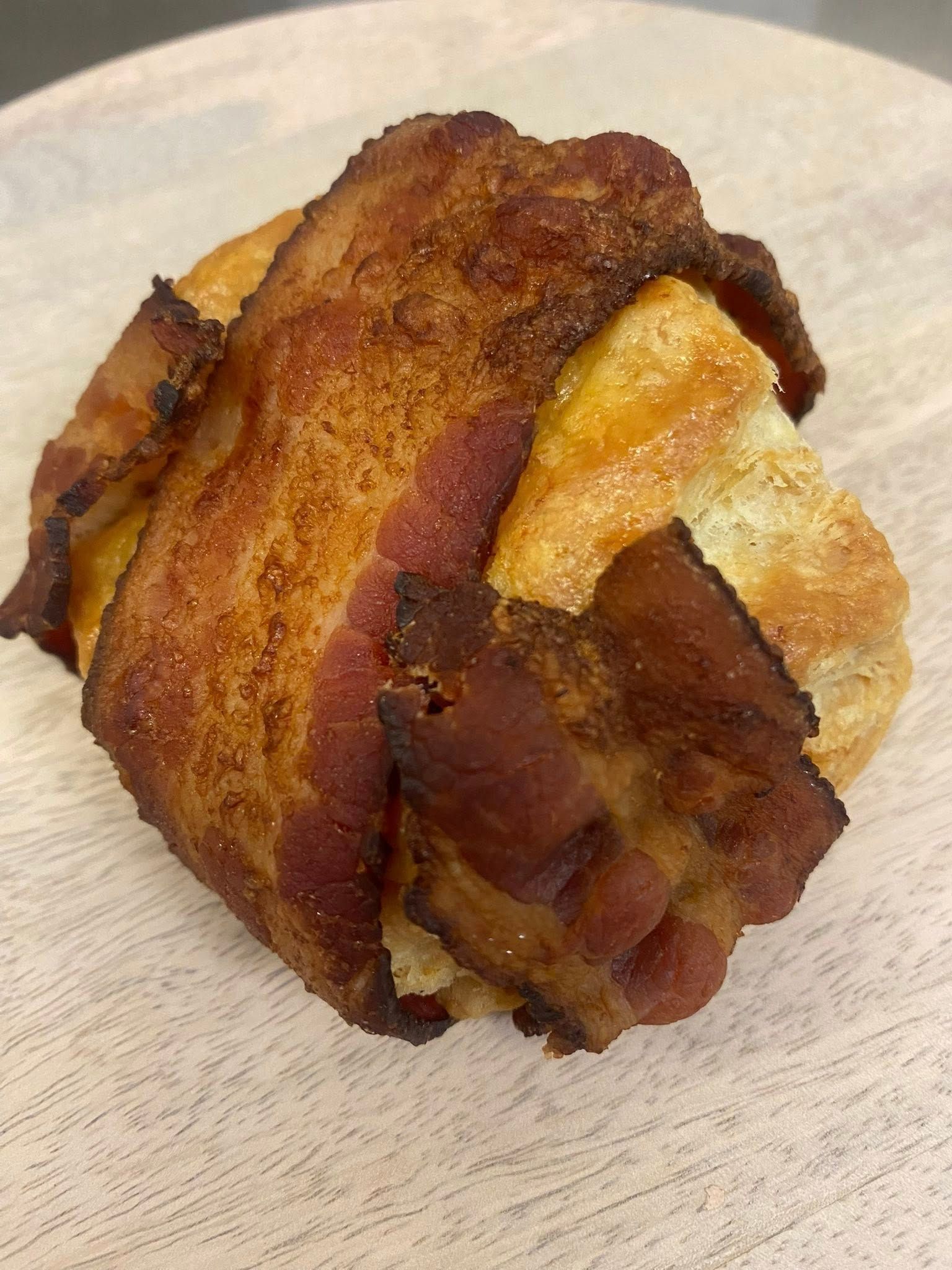 Bacon-wrapped pastry on a white surface; bacon is crispy, brown, and partially covers the golden-brown pastry.