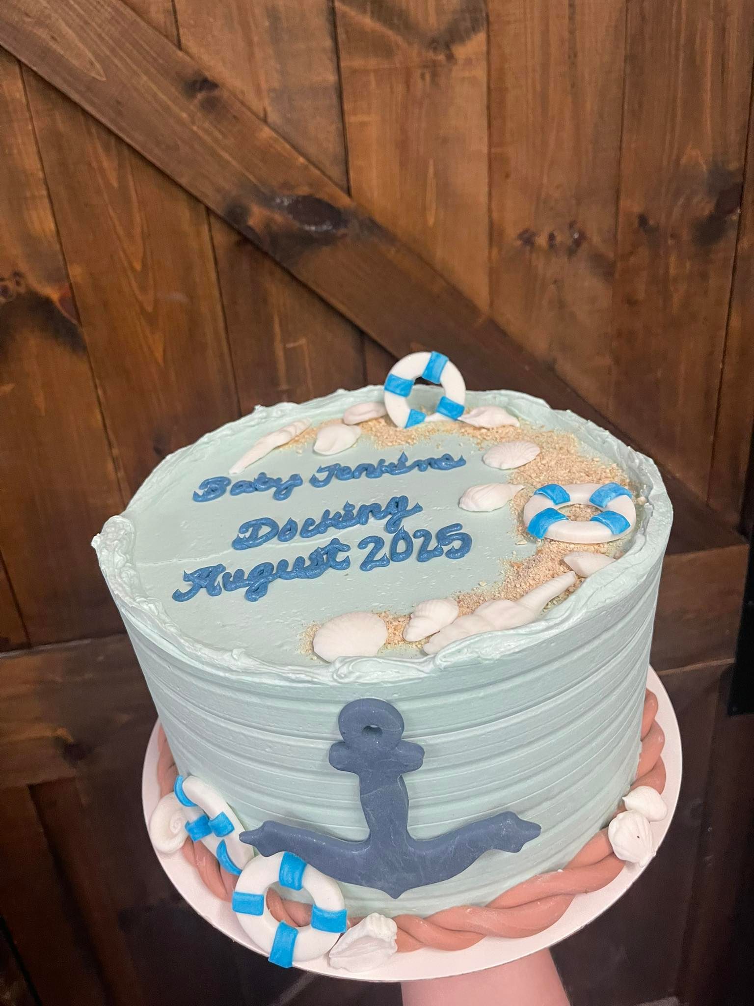 Cake decorated with anchor, life preservers, sand, and blue frosting, announcing 