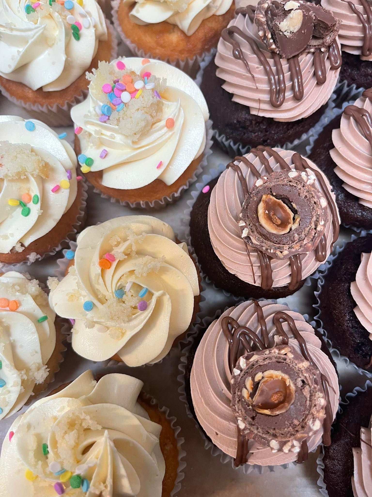 Cupcakes with various frosting and toppings: sprinkles, chocolate drizzle, nuts.