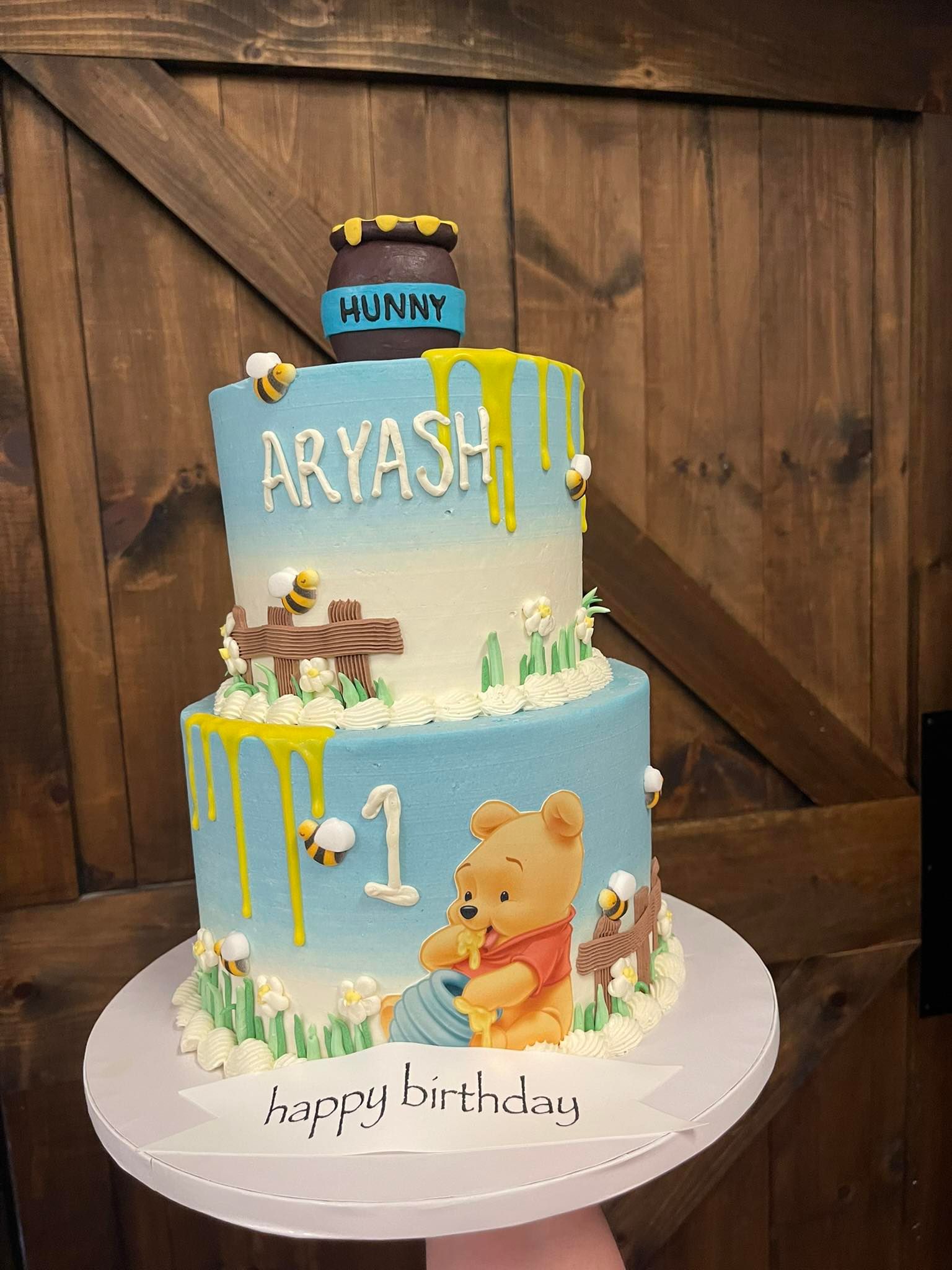 Two-tiered Winnie the Pooh birthday cake with honey pot, name, bees, and 