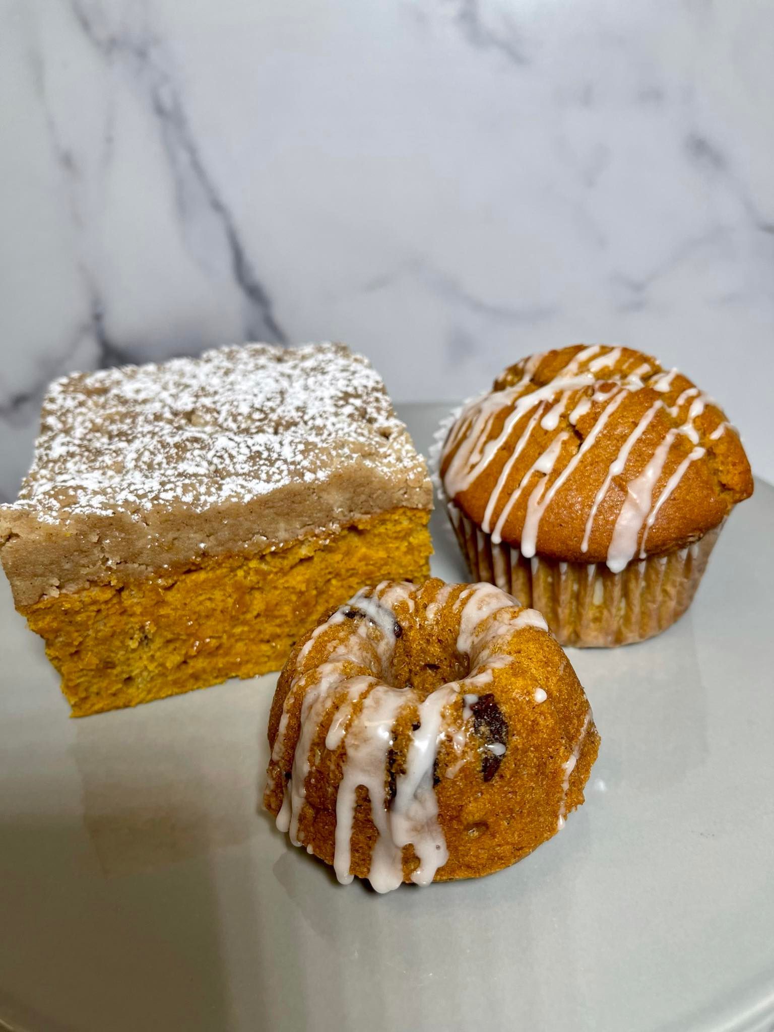 Three baked goods: a frosted cake square, a muffin with icing drizzle, and a mini Bundt cake with icing.