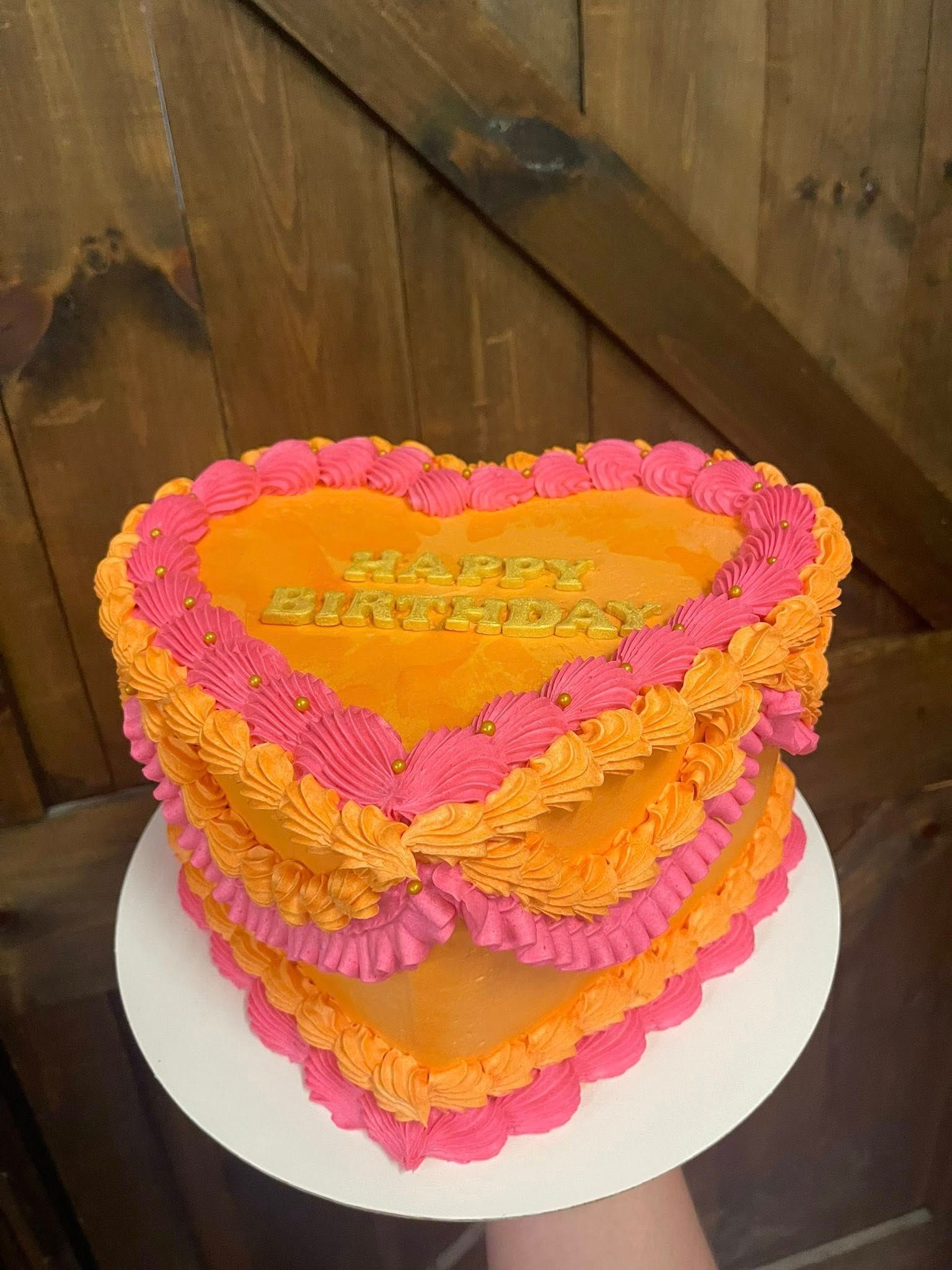 Two-tiered heart-shaped cake with orange frosting, pink trim, and 