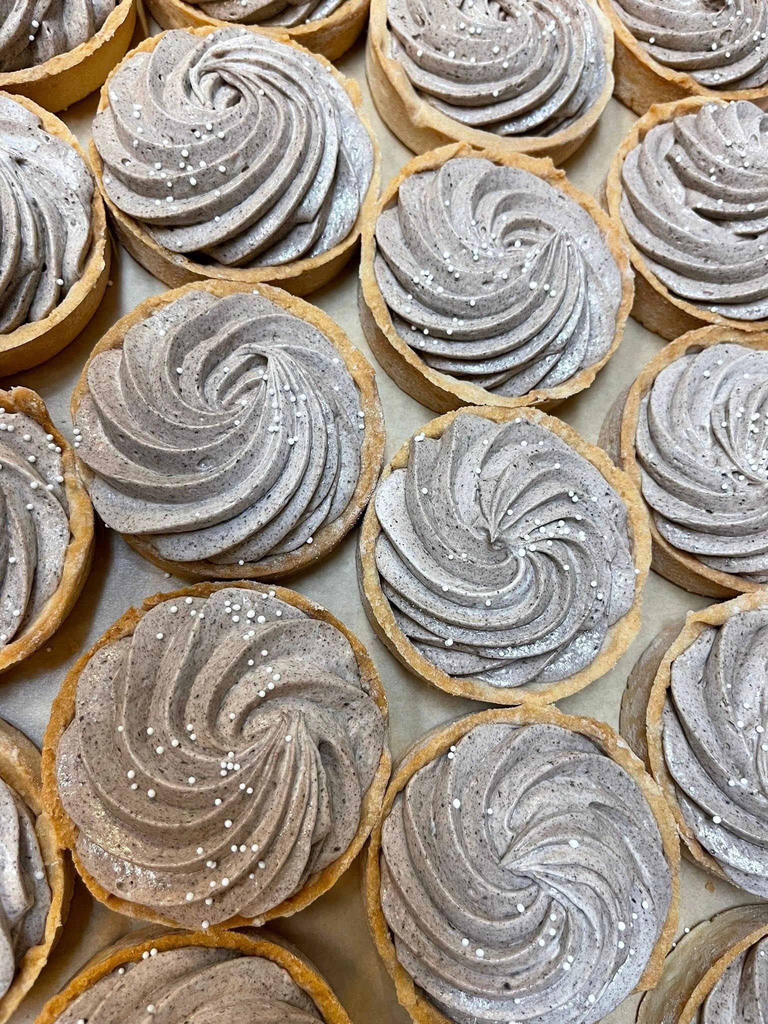 Mini tarts with swirled gray frosting, dusted with white powder, in a baking tray.