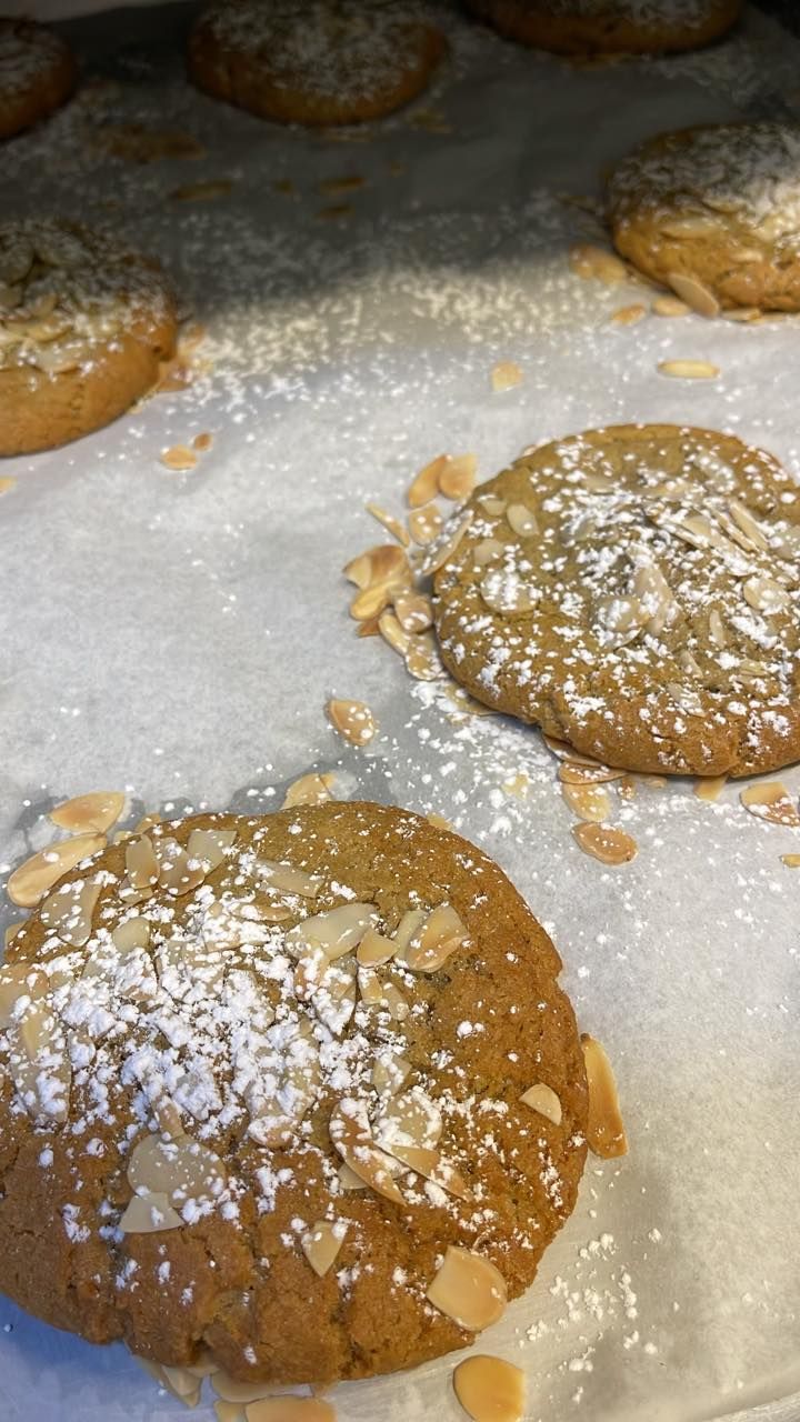 Cookies on parchment paper, dusted with powdered sugar and almond slivers.