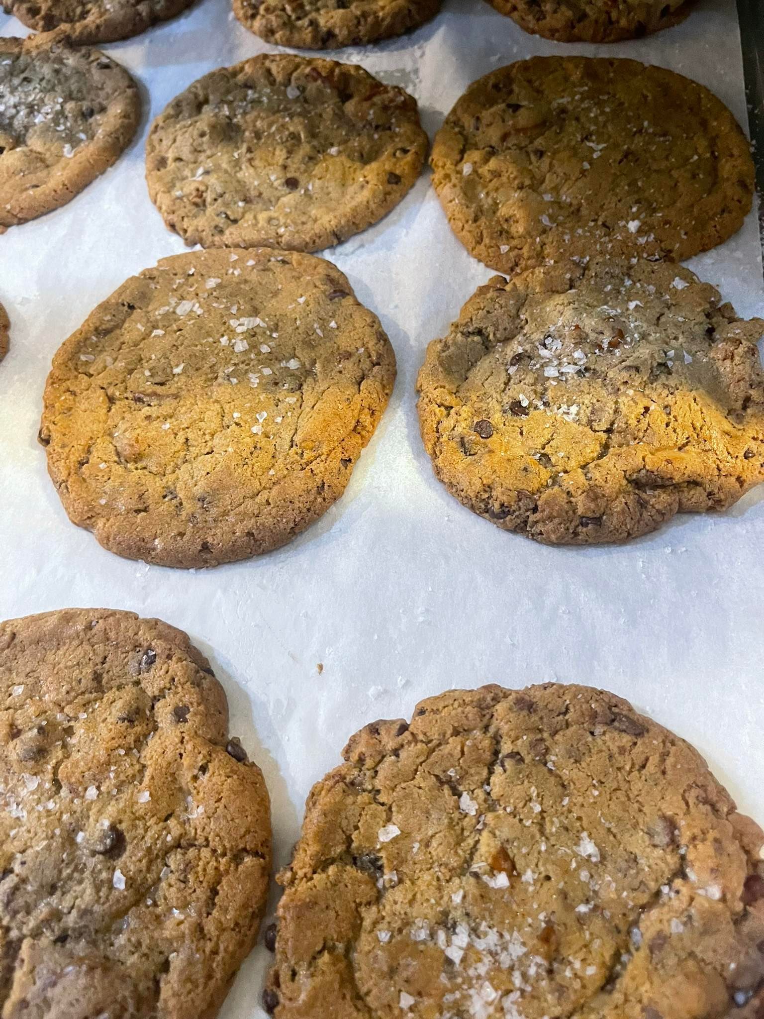 Close-up of freshly baked chocolate chip cookies with flaky sea salt on parchment paper.