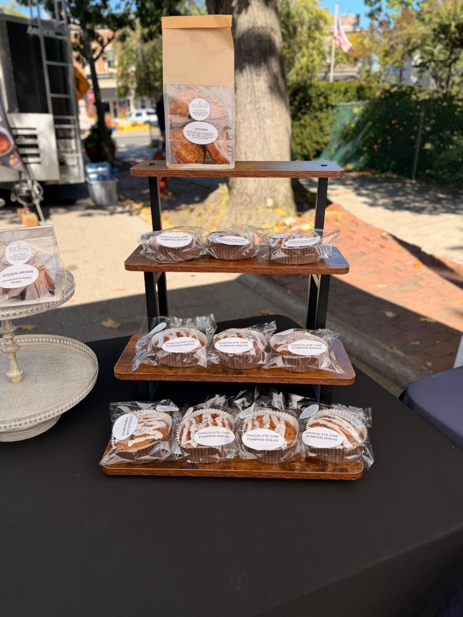 Baked goods display at a market, with tiered wooden shelves holding wrapped pastries and a paper bag.
