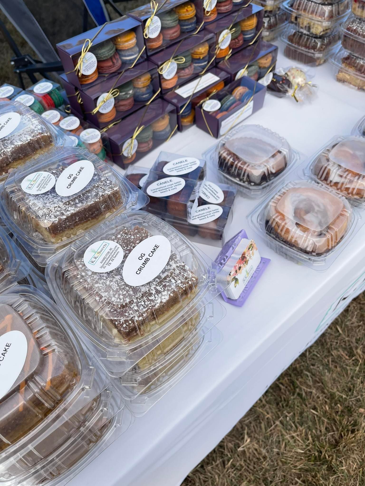 Baked goods on display at an outdoor market, various cakes and cookies, packaged for sale.