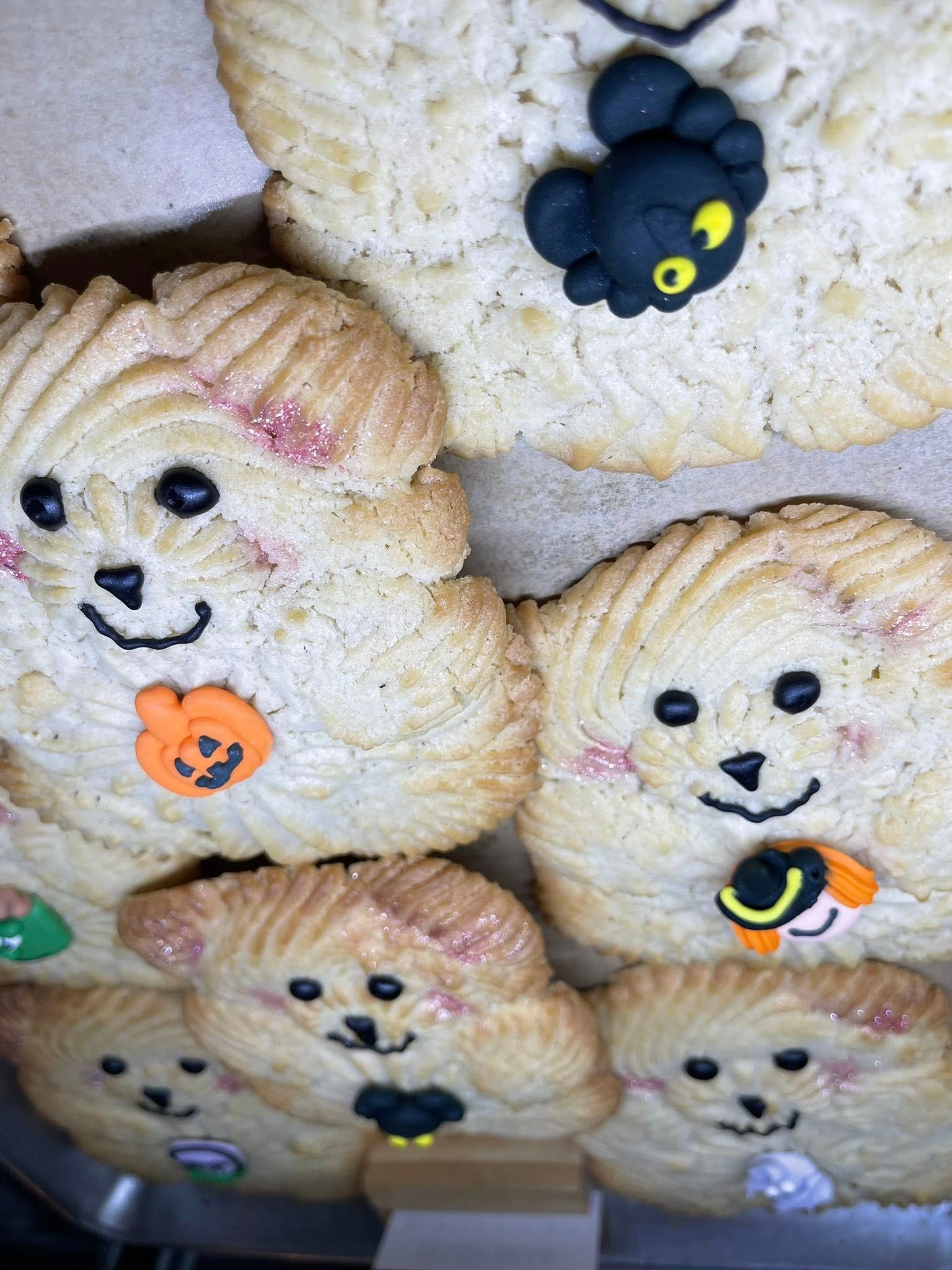 Close-up of dog-shaped cookies decorated with black eyes, pink cheeks, and Halloween-themed accessories.