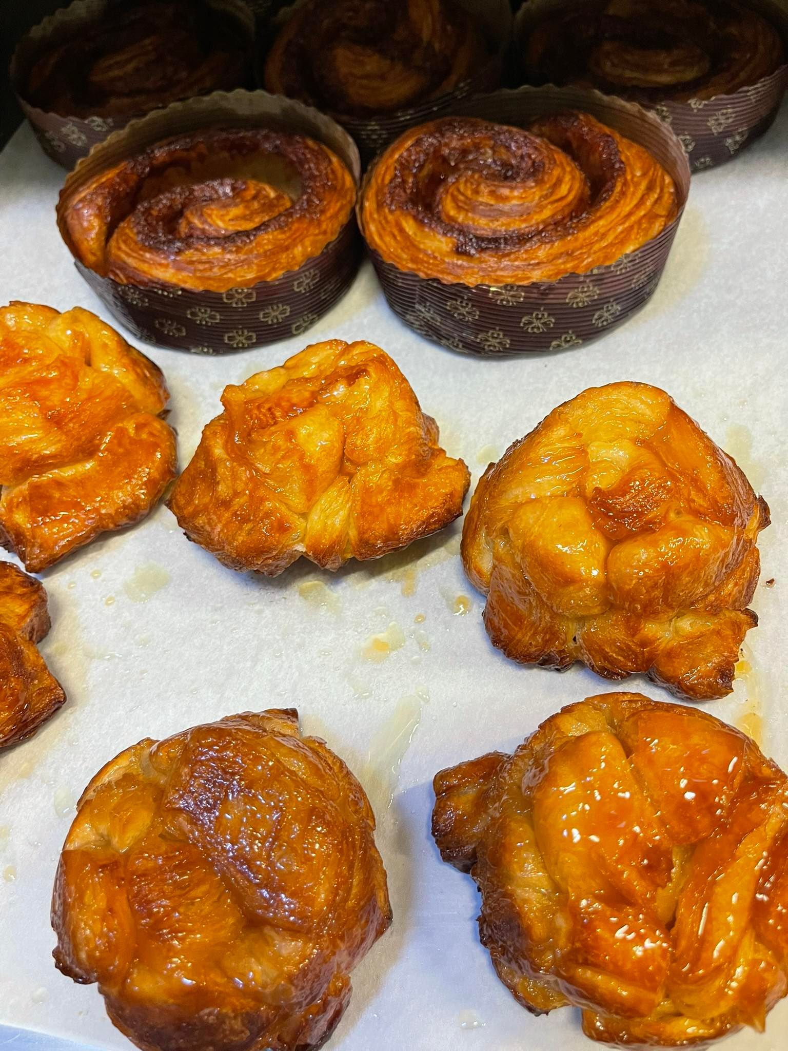 Pastries, two cinnamon rolls and several caramelized, golden-brown baked goods on white paper.