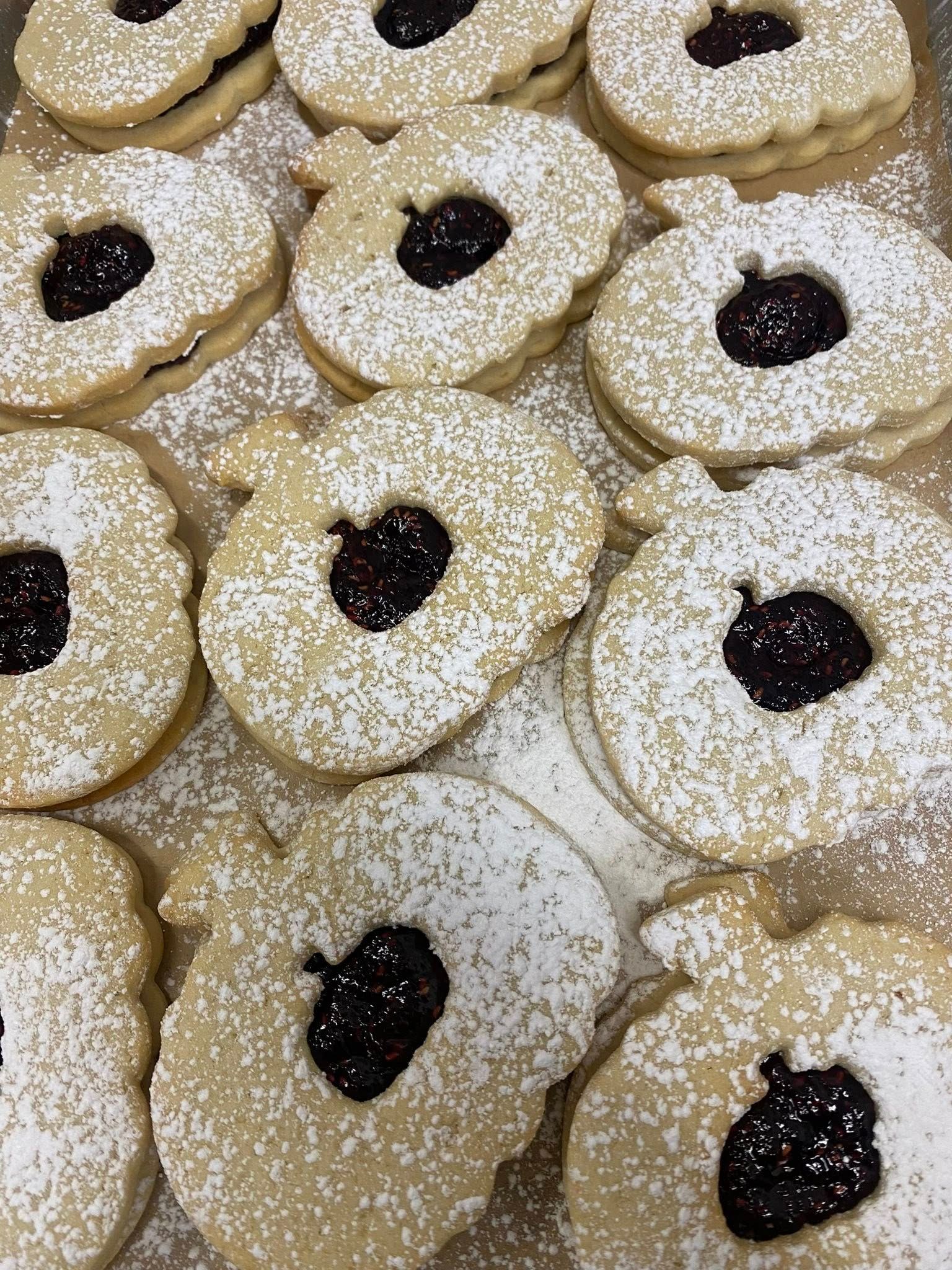 Pumpkin-shaped sandwich cookies filled with dark jam, dusted with powdered sugar, arranged on a tray.