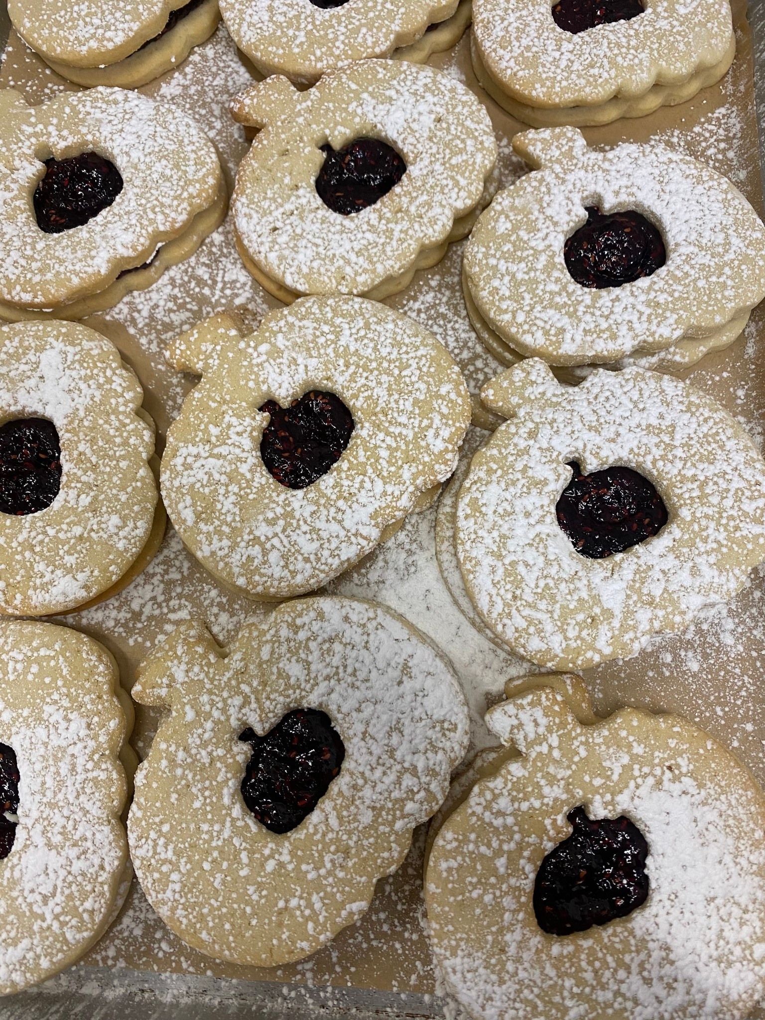 Pumpkin-shaped cookies with jam centers dusted with powdered sugar on a tray.