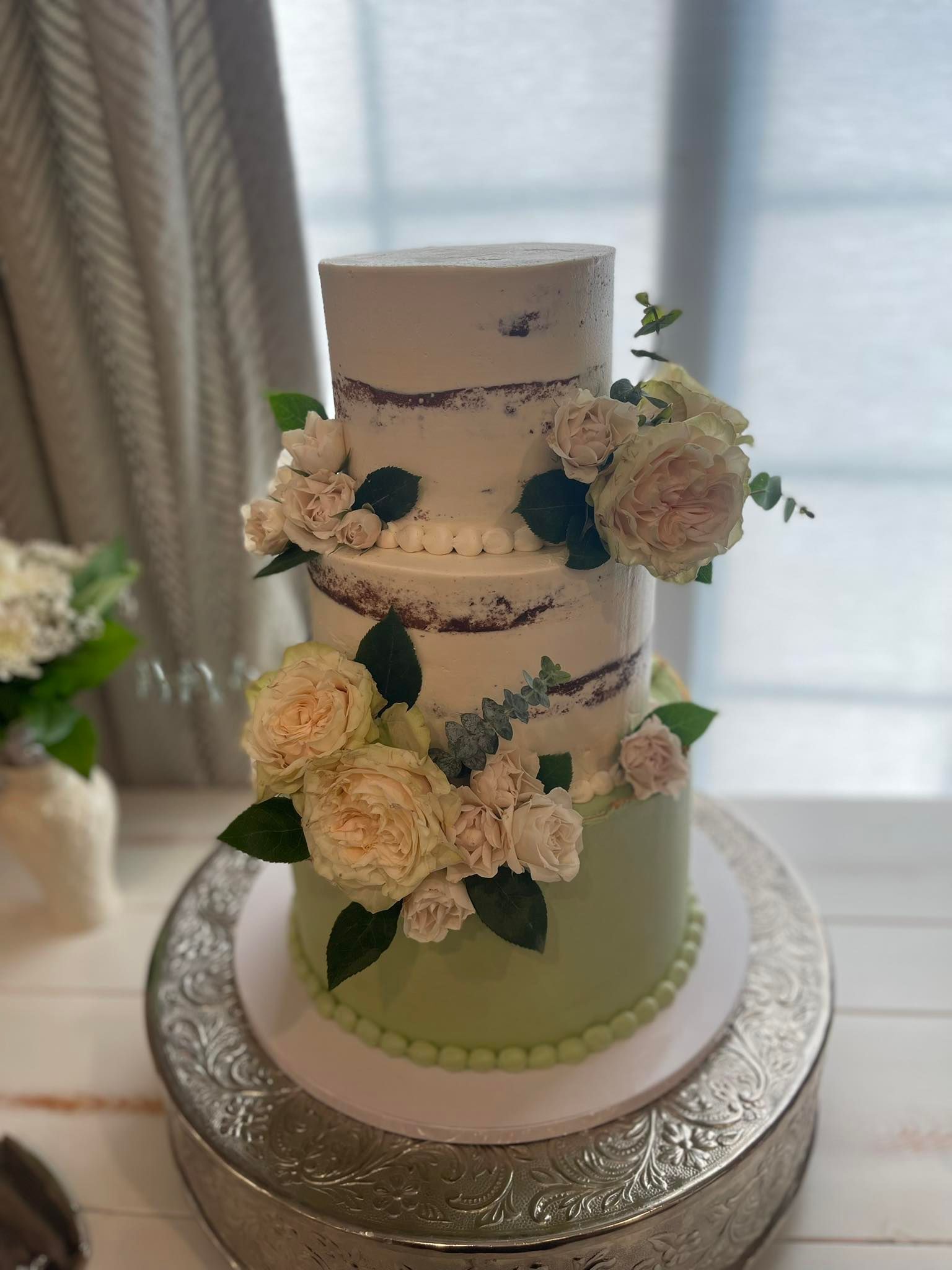 Three-tiered cake decorated with flowers and green frosting on the bottom tier.