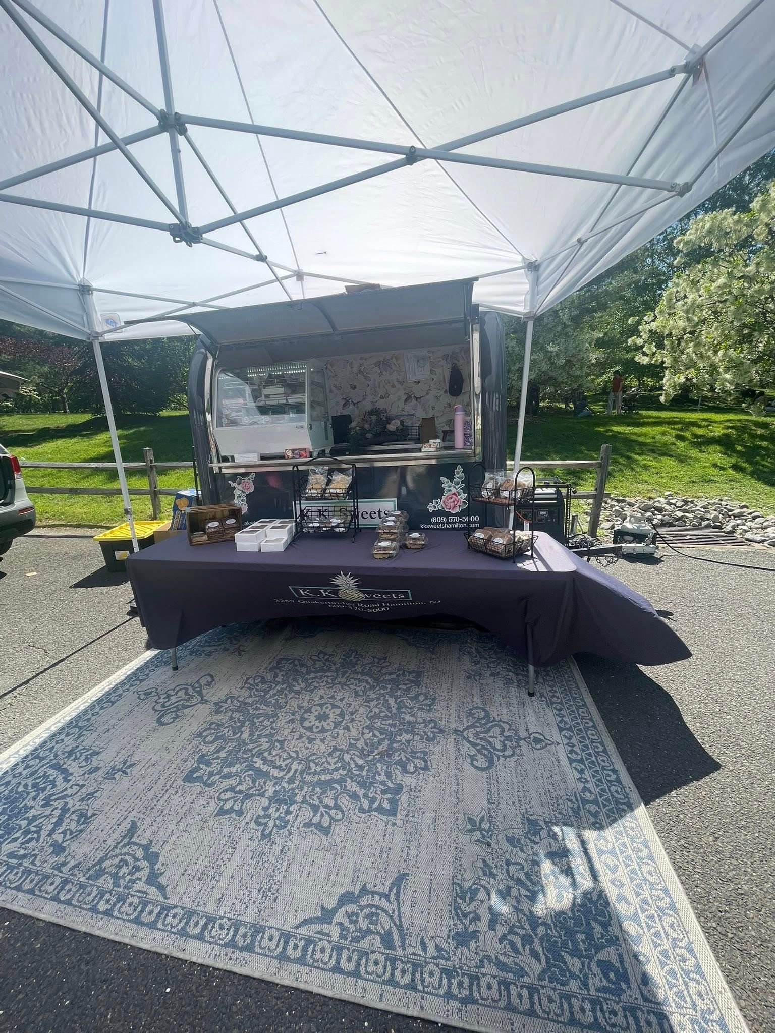 A vendor booth under a canopy, displaying jewelry on a purple table, set on a patterned rug outdoors.