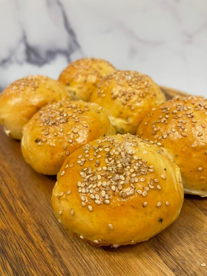 Seven golden, sesame-topped hamburger buns on a wooden cutting board, close-up shot.