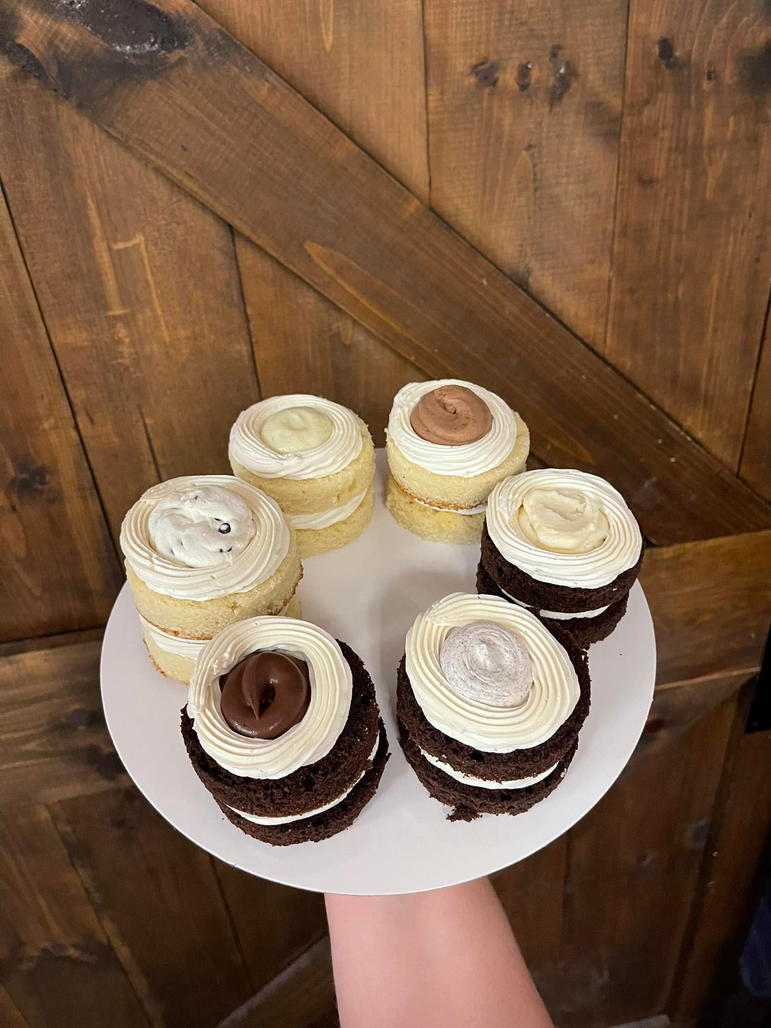 Plate of mini cakes with various toppings, held against a wood door.