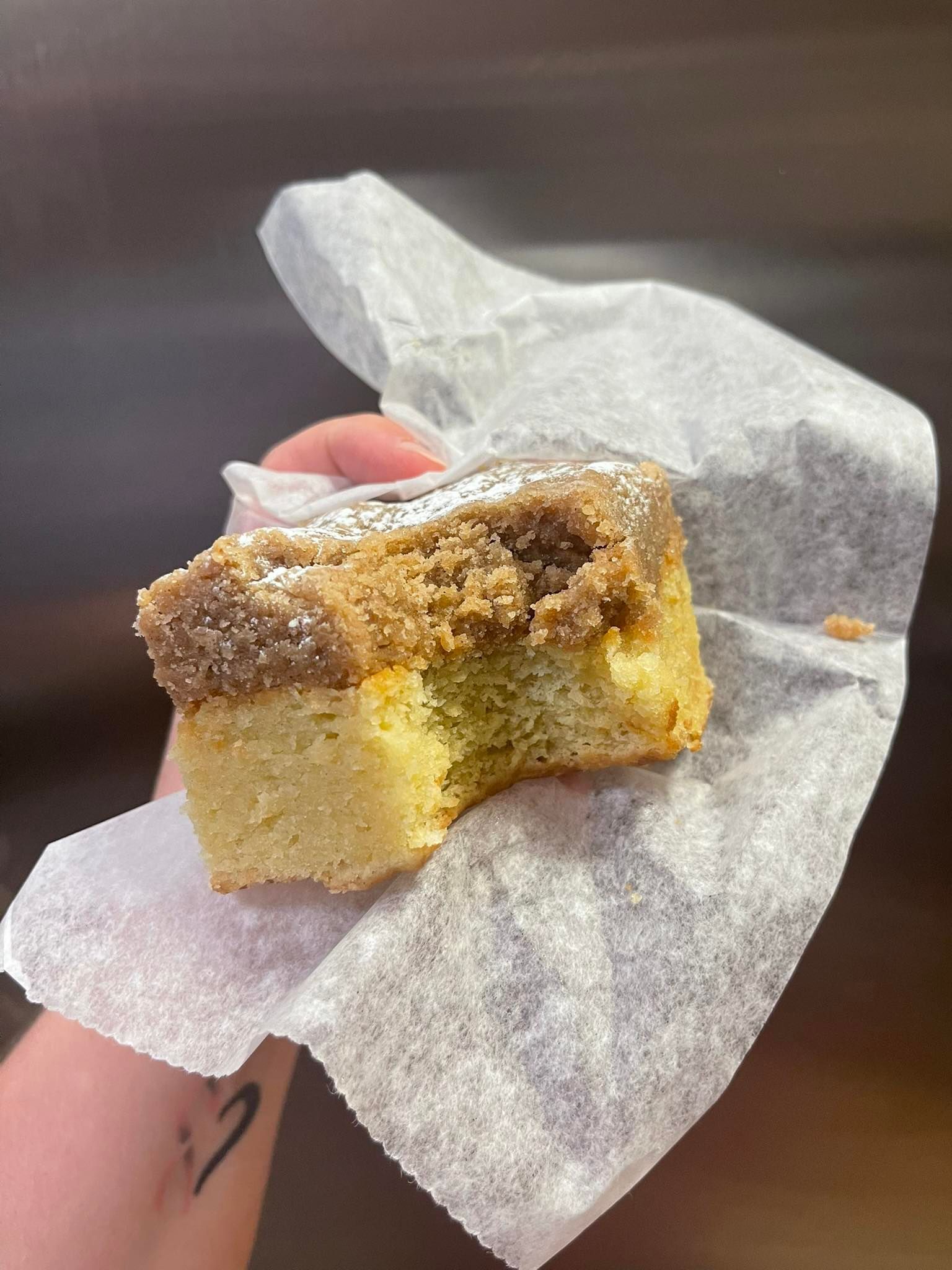 Person holding a partially eaten slice of coffee cake in parchment paper.