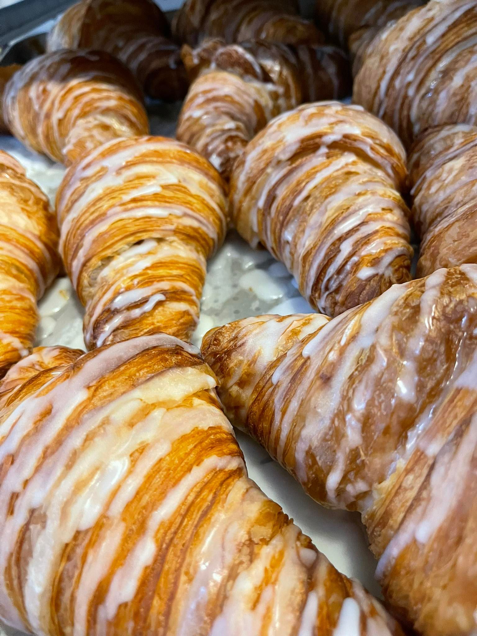 Glazed croissants, golden brown with white icing, arranged closely together.