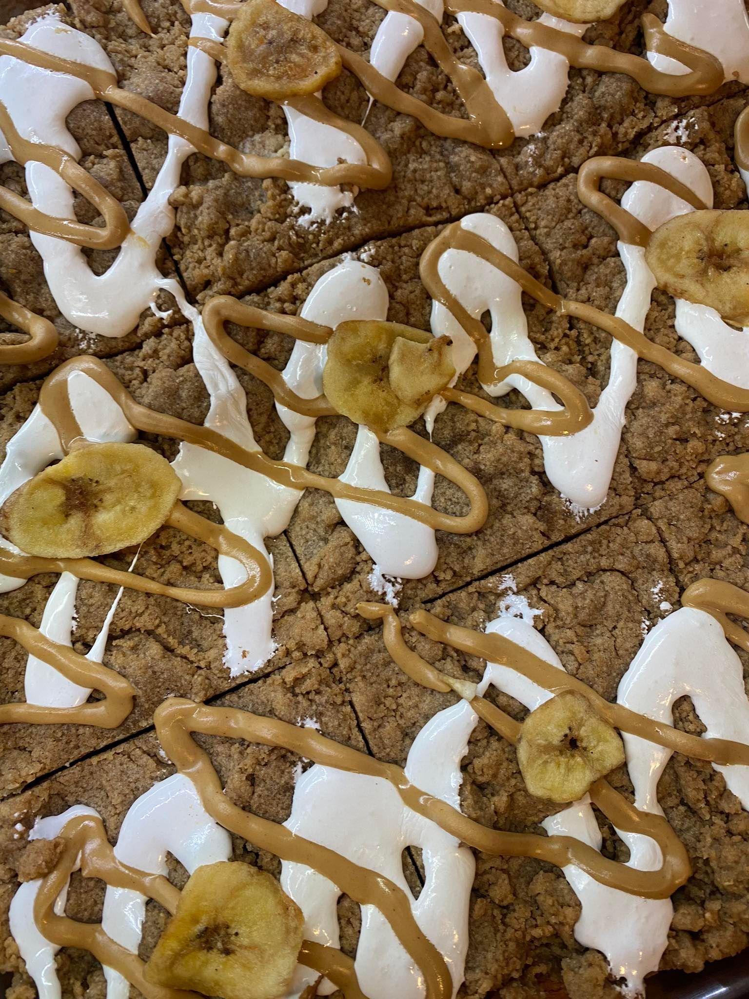 Overhead view of dessert bars with peanut butter and white icing drizzled, topped with banana chips.