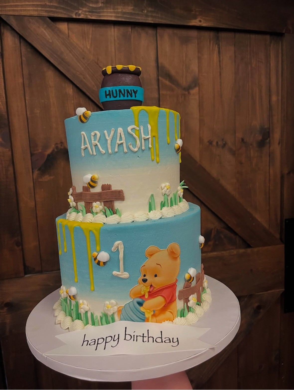 Two-tiered Winnie the Pooh birthday cake, blue and white with honey details, bees, and the name 