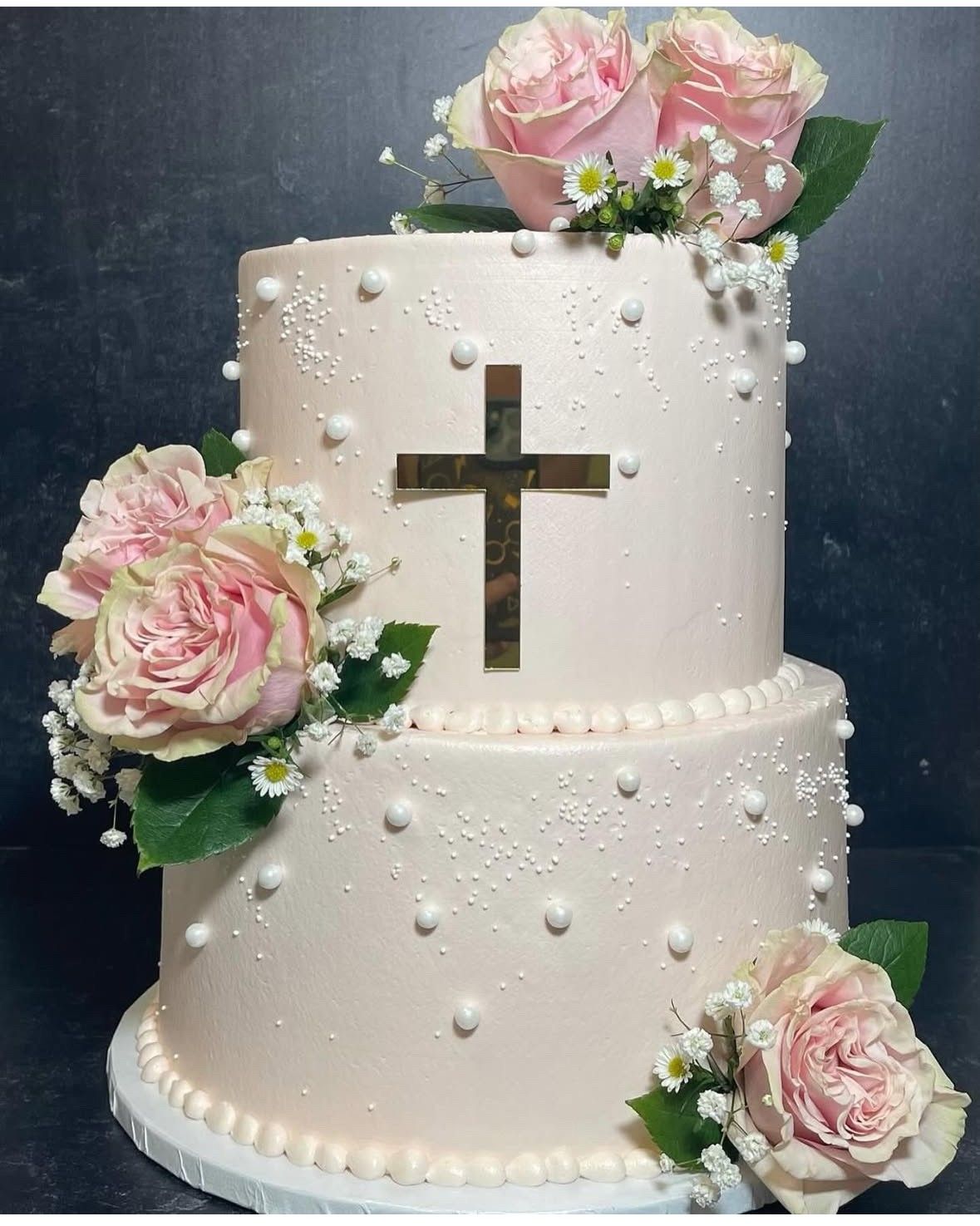 Two-tiered pink cake with gold cross and pink rose decorations.
