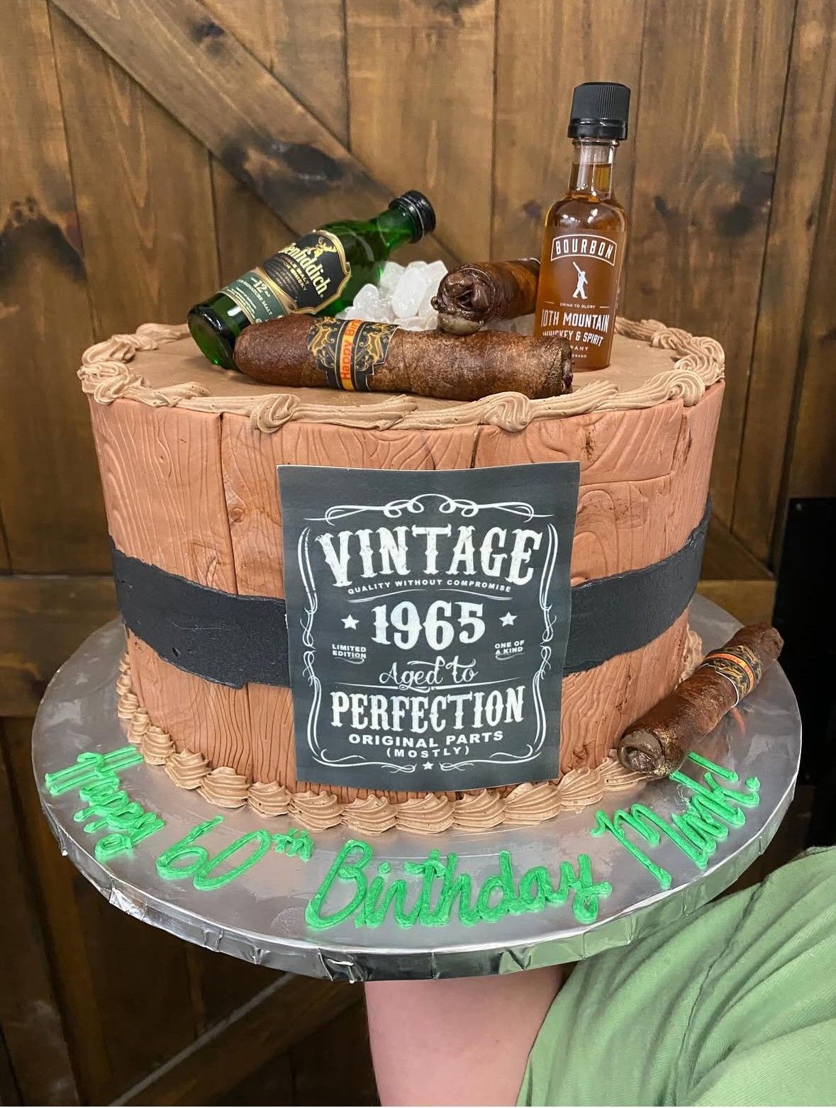 Cake decorated as a whiskey barrel with cigars and bottles on top; says 