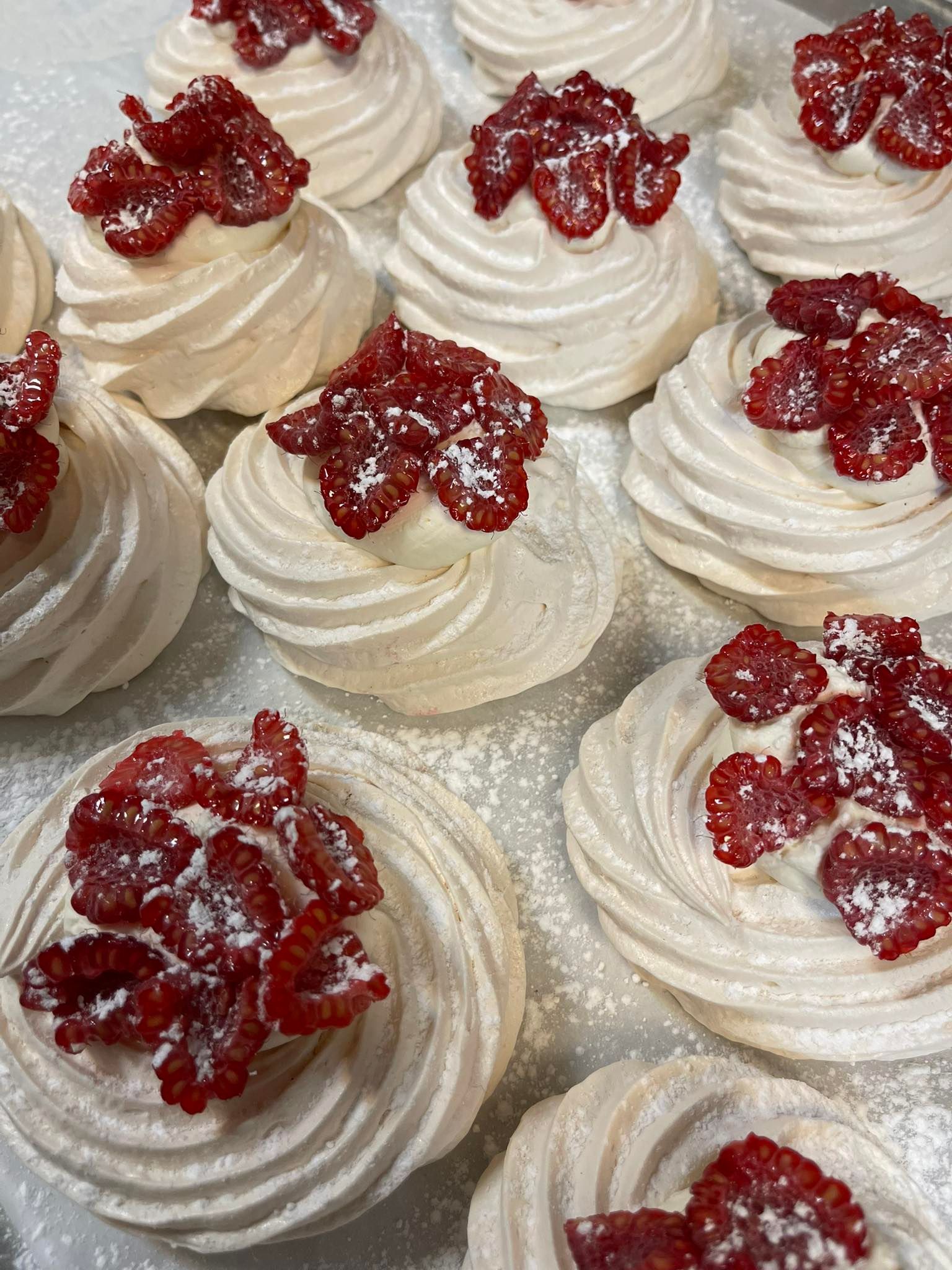 Close-up of meringue nests topped with red berries and powdered sugar.