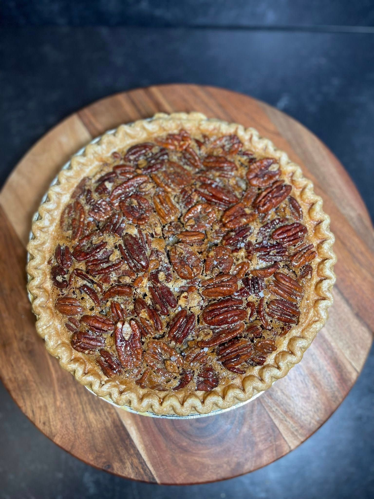 Pecan pie on a wooden board; crust is golden brown and filled with pecans and caramelized sugar.