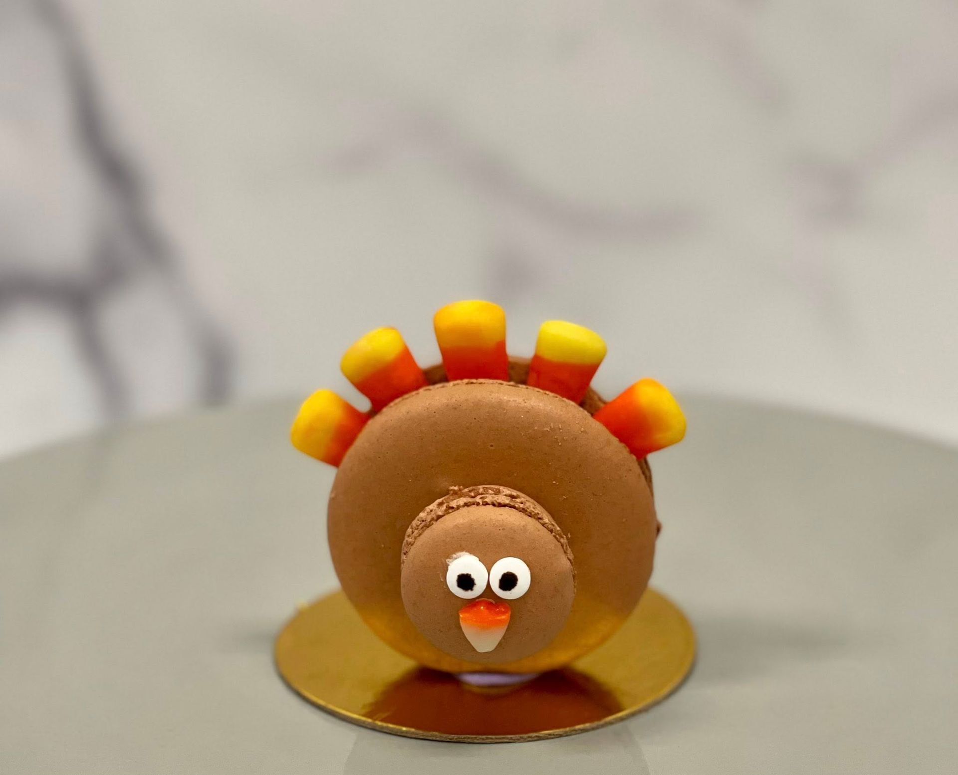 Macaron turkey on a gold plate, brown body, candy corn feathers, and a small face.